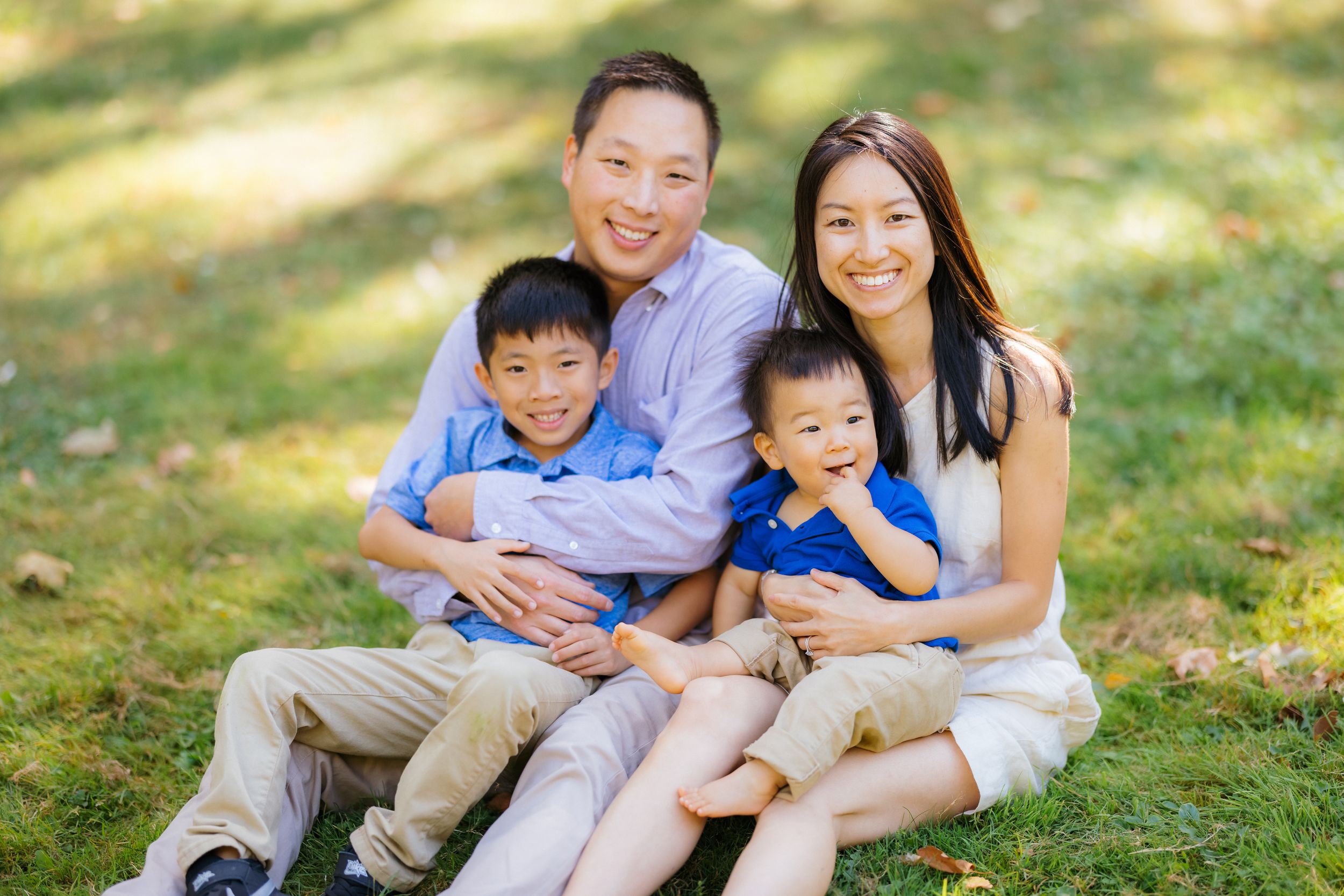 A family of four sits together on grass for an outdoor portrait.