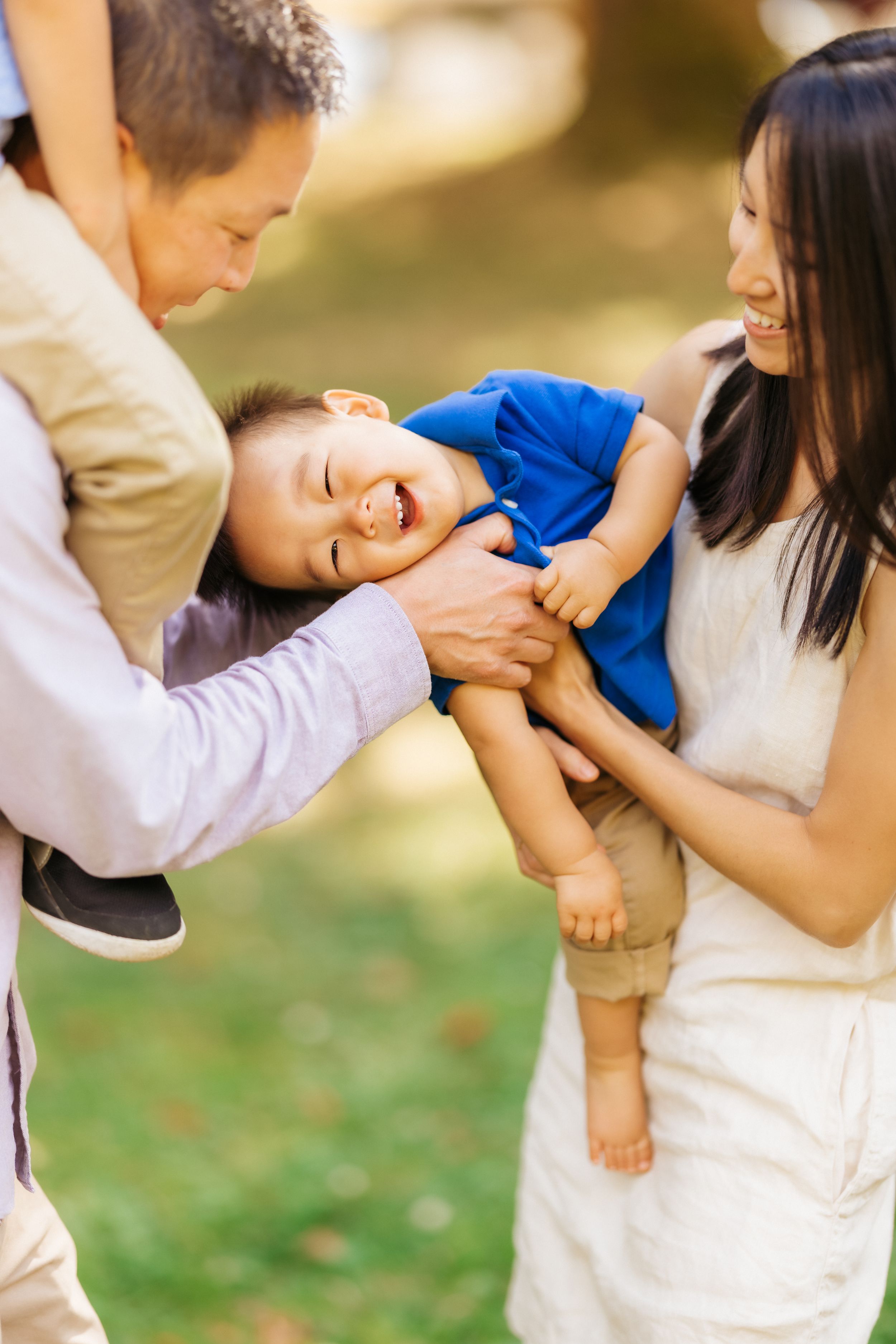 A family plays and laughs together in a park on a sunny afternoon.
