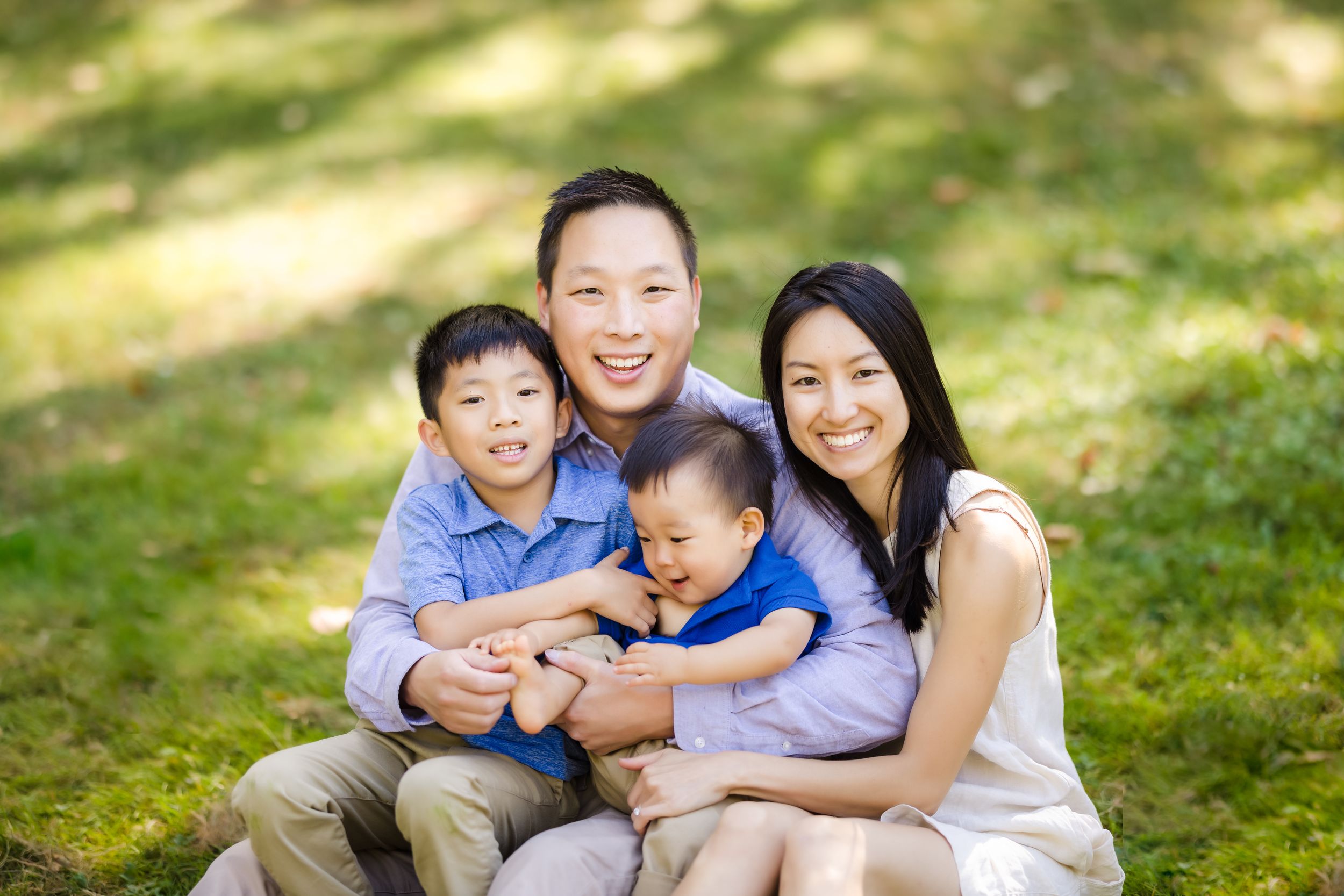 A loving family of four sits together on grass during an outdoor photo session.