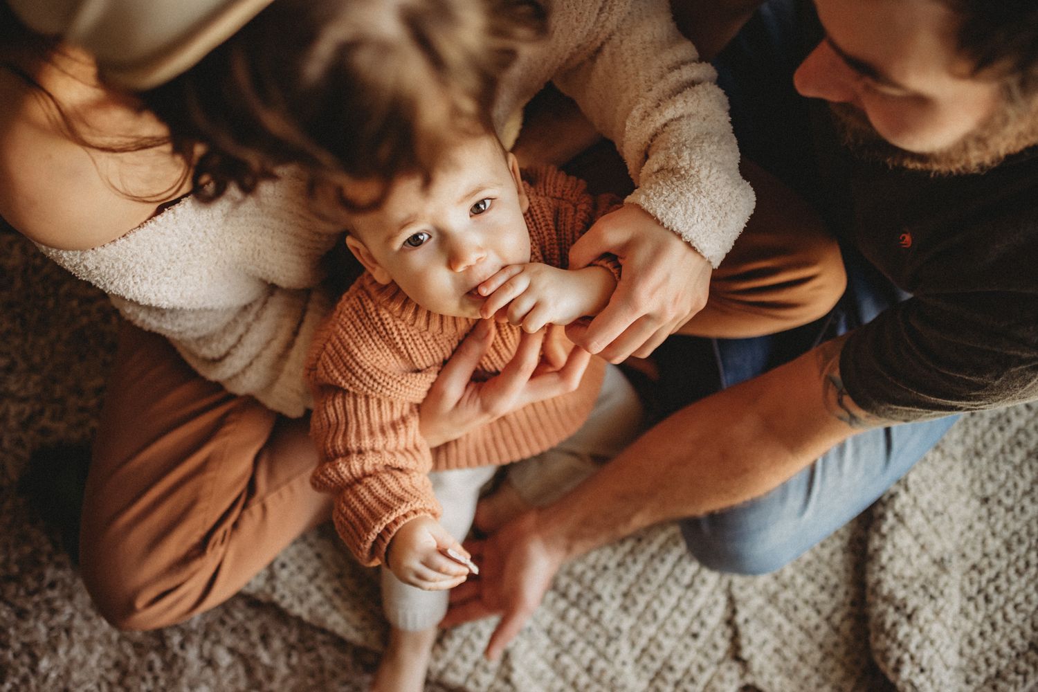 Overhead view of parents playing with their baby on a cozy carpet.