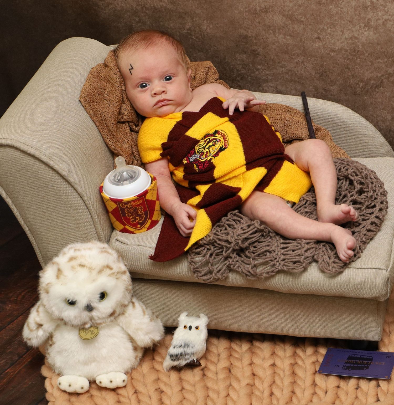 A baby in maroon and gold sports attire reclines on a beige couch with plush toys.