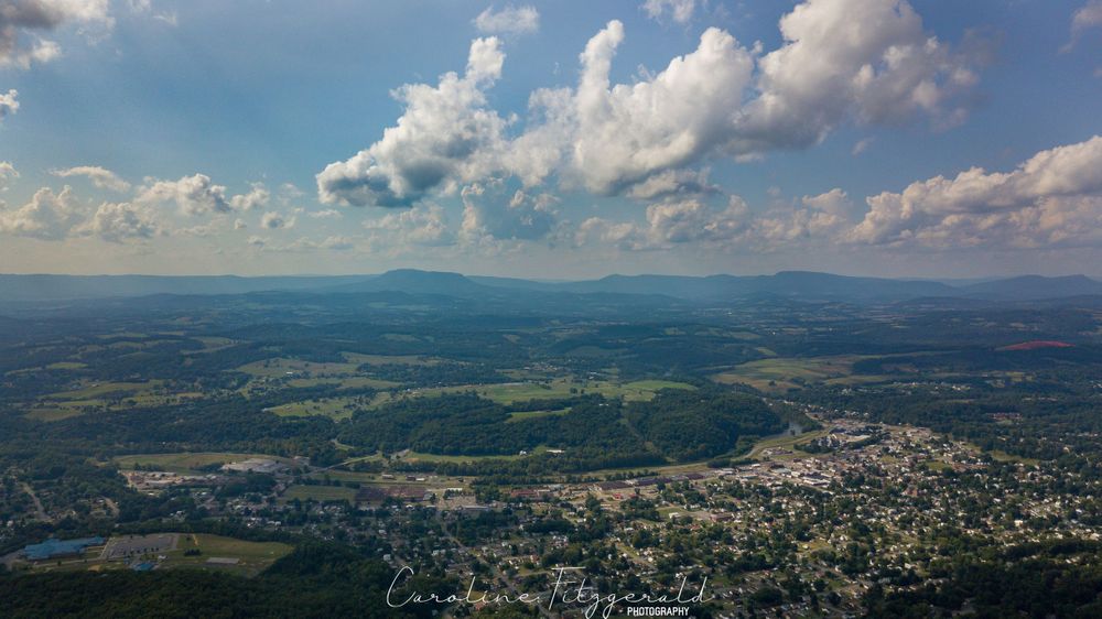Aerial view of a mountain valley with puffy white clouds and blue skies over green terrain.