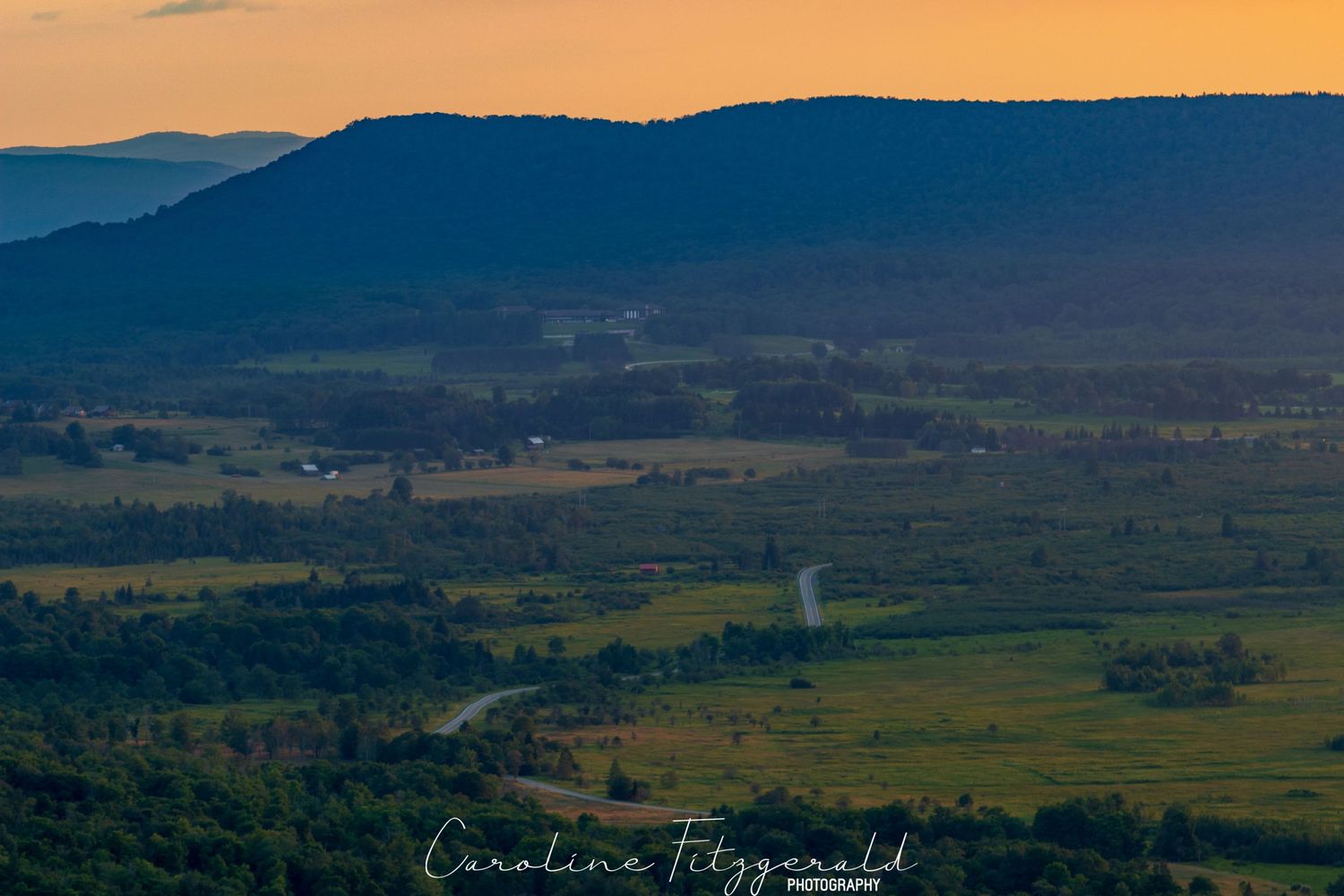 Aerial view of rolling hills and farmland at sunset with mountains in the distance.