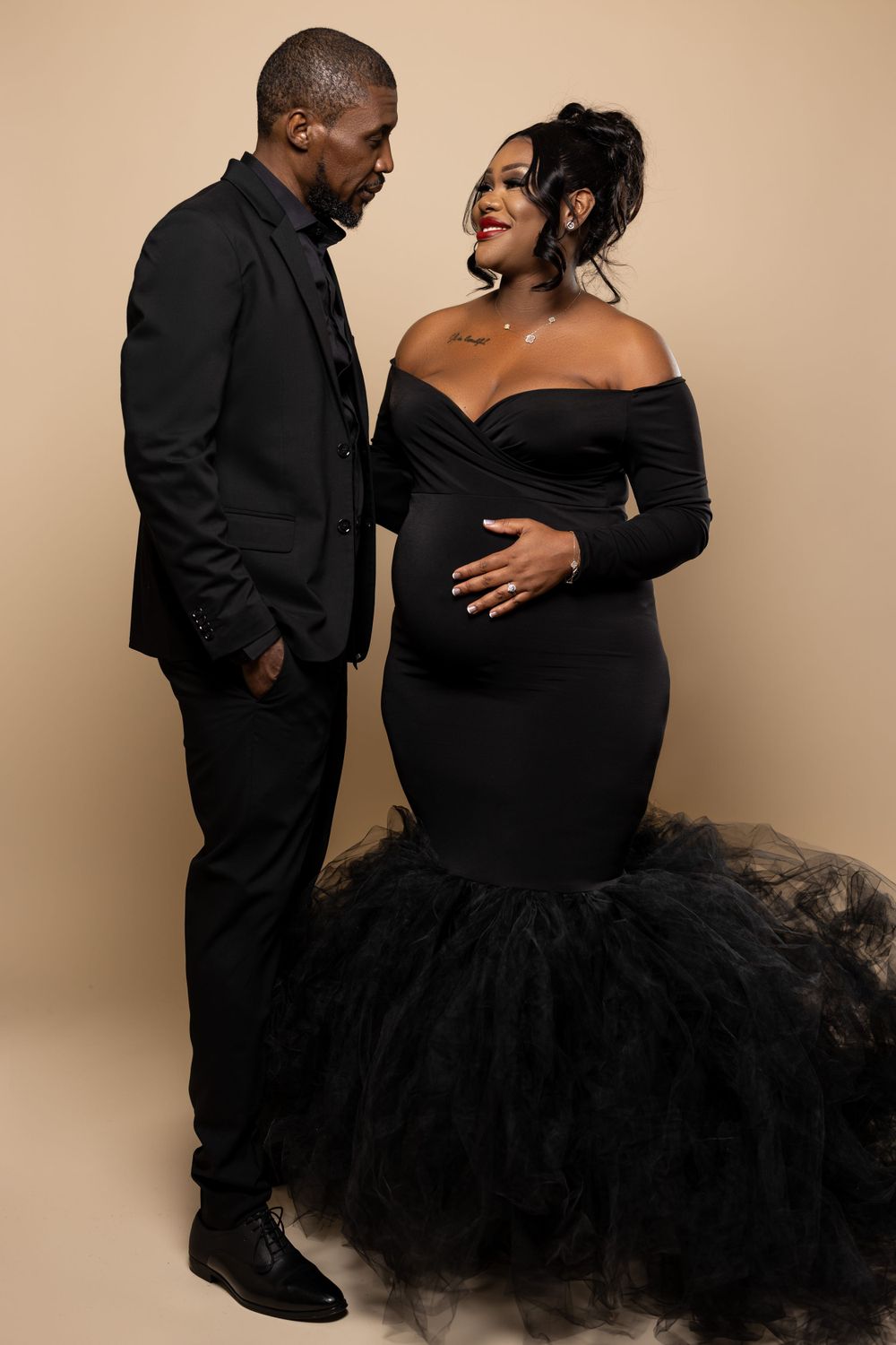 Elegant maternity photoshoot featuring couple in formal black attire.