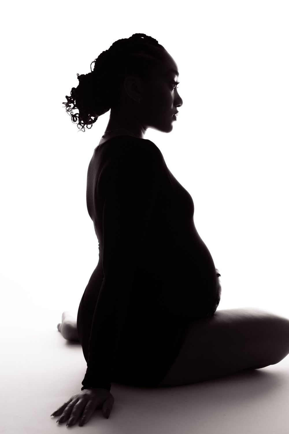 Artistic silhouette of an expectant mother seated in a graceful pose against a white background.