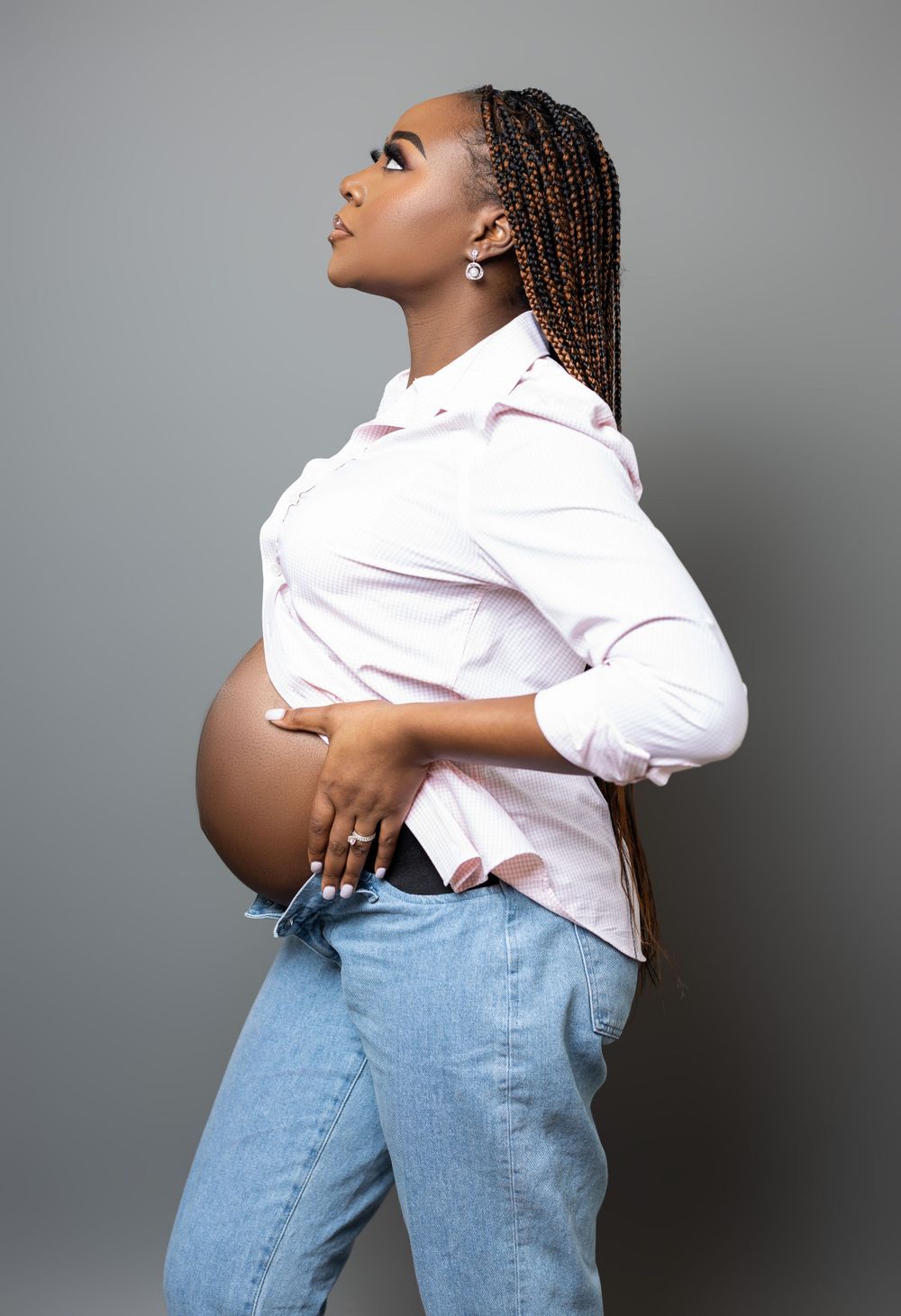 Side profile maternity shot showing pregnant belly in white shirt and jeans.
