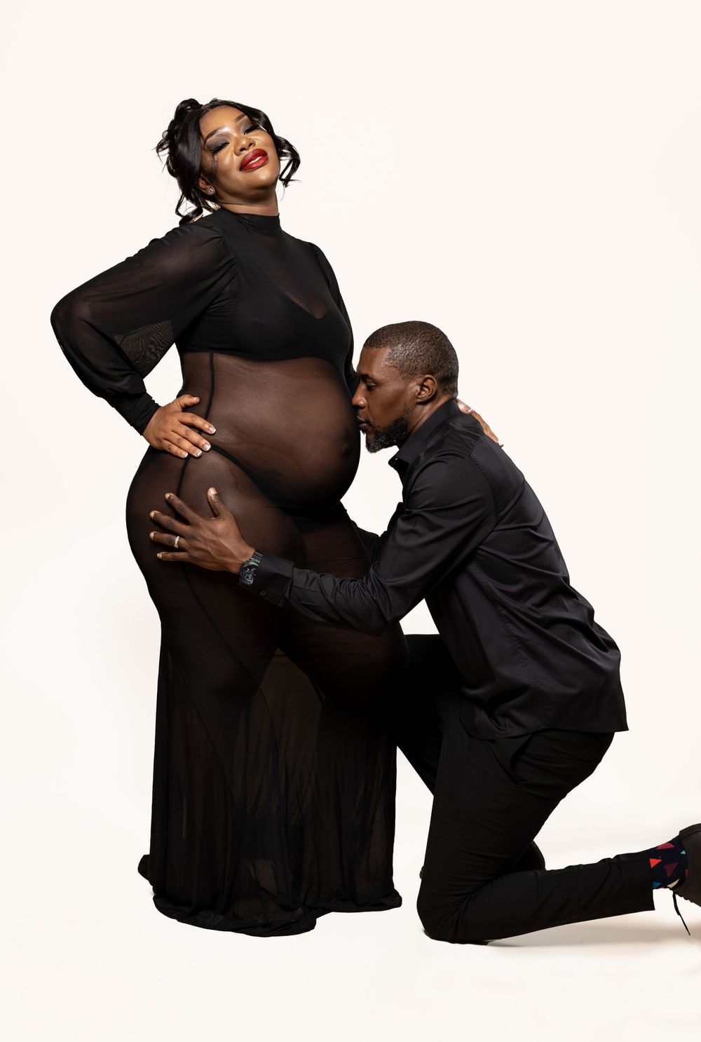 Artistic maternity portrait with couple in black clothing against white backdrop.