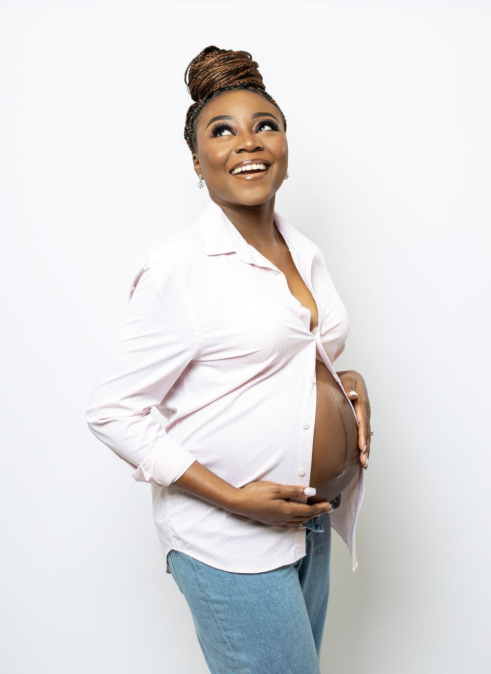 Candid maternity portrait in white button-down shirt and jeans against white background.