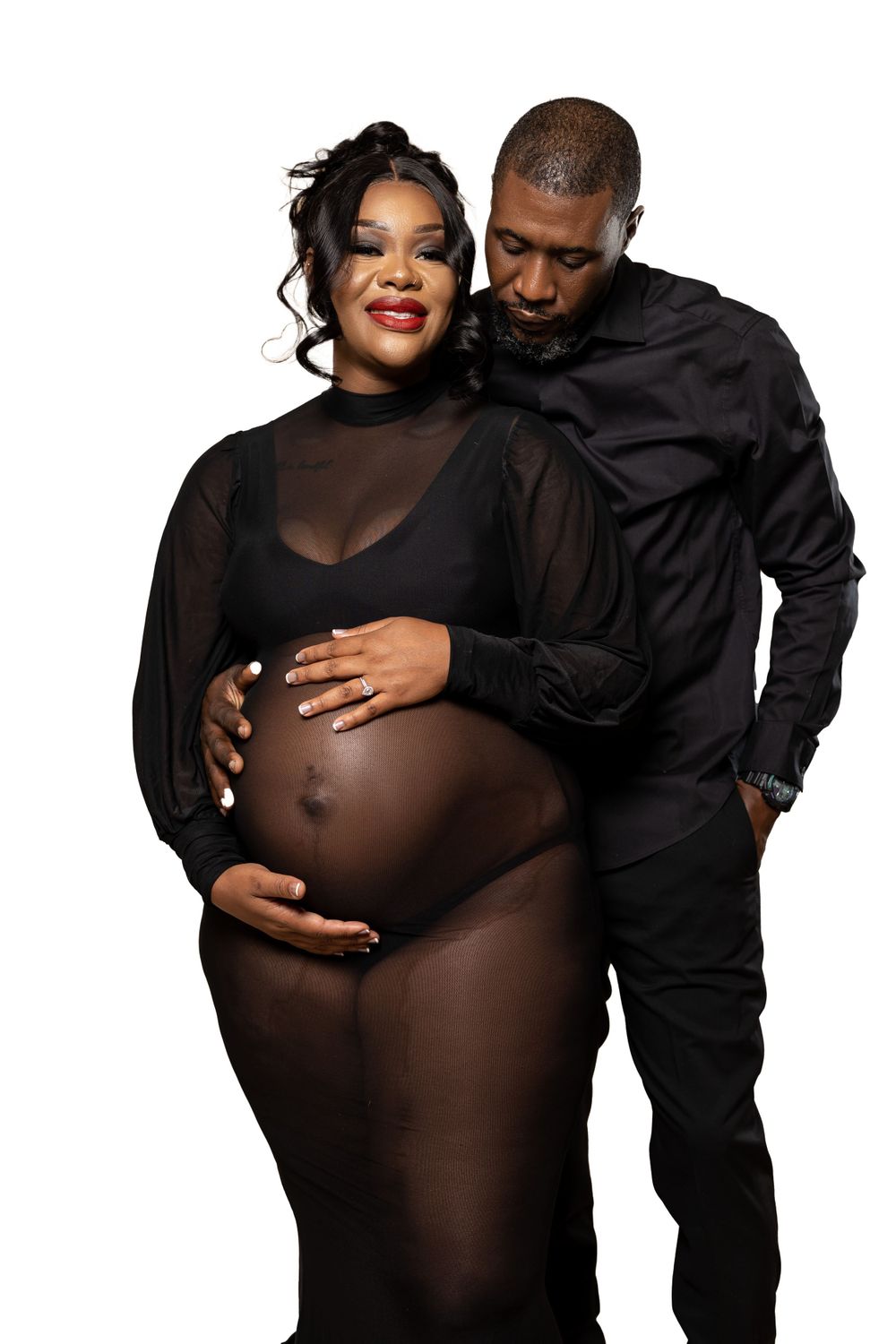 Intimate maternity photo of couple in black attire against dark background.