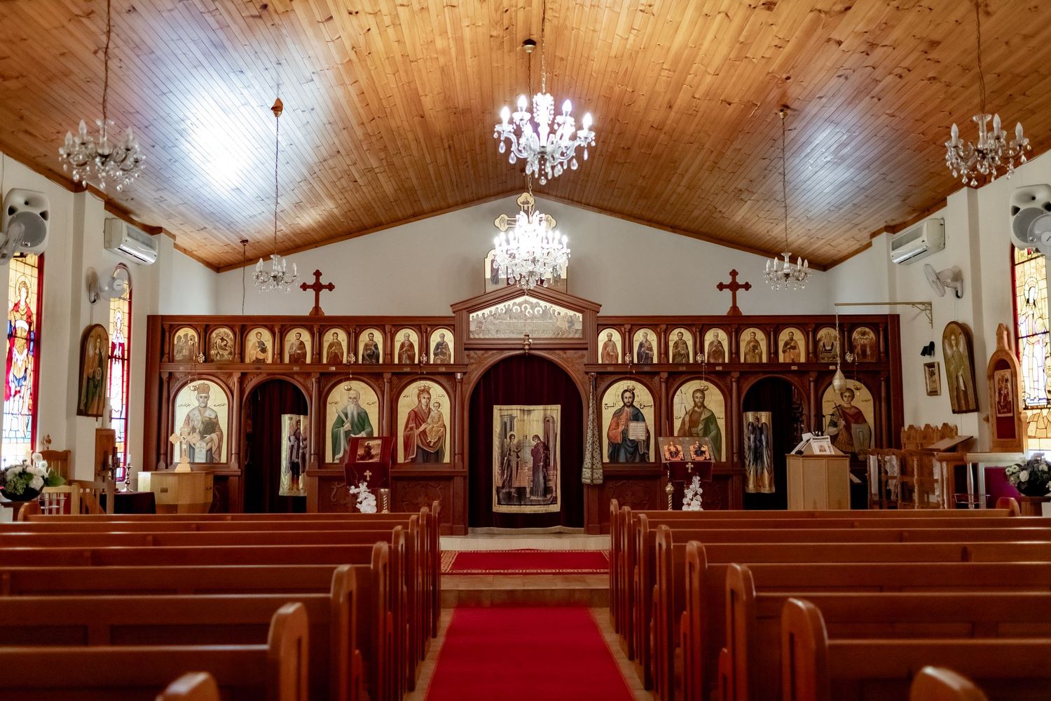Interior of an ornate church with wooden ceiling, crystal chandeliers, and religious iconography.
