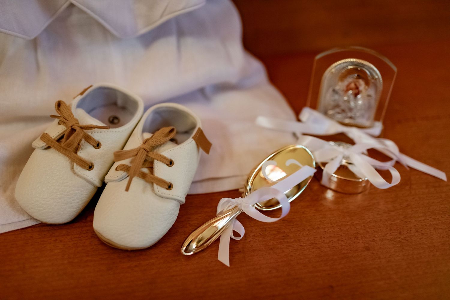 Small white baby shoes with brown laces displayed next to a small decorative frame on a wooden surface.