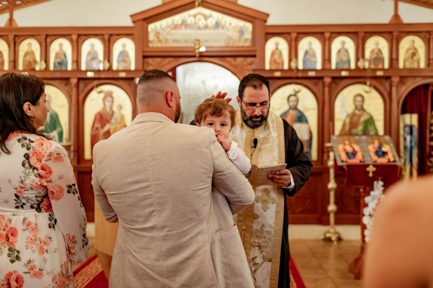 Orthodox Christian baptism ceremony being performed in front of traditional iconostasis.