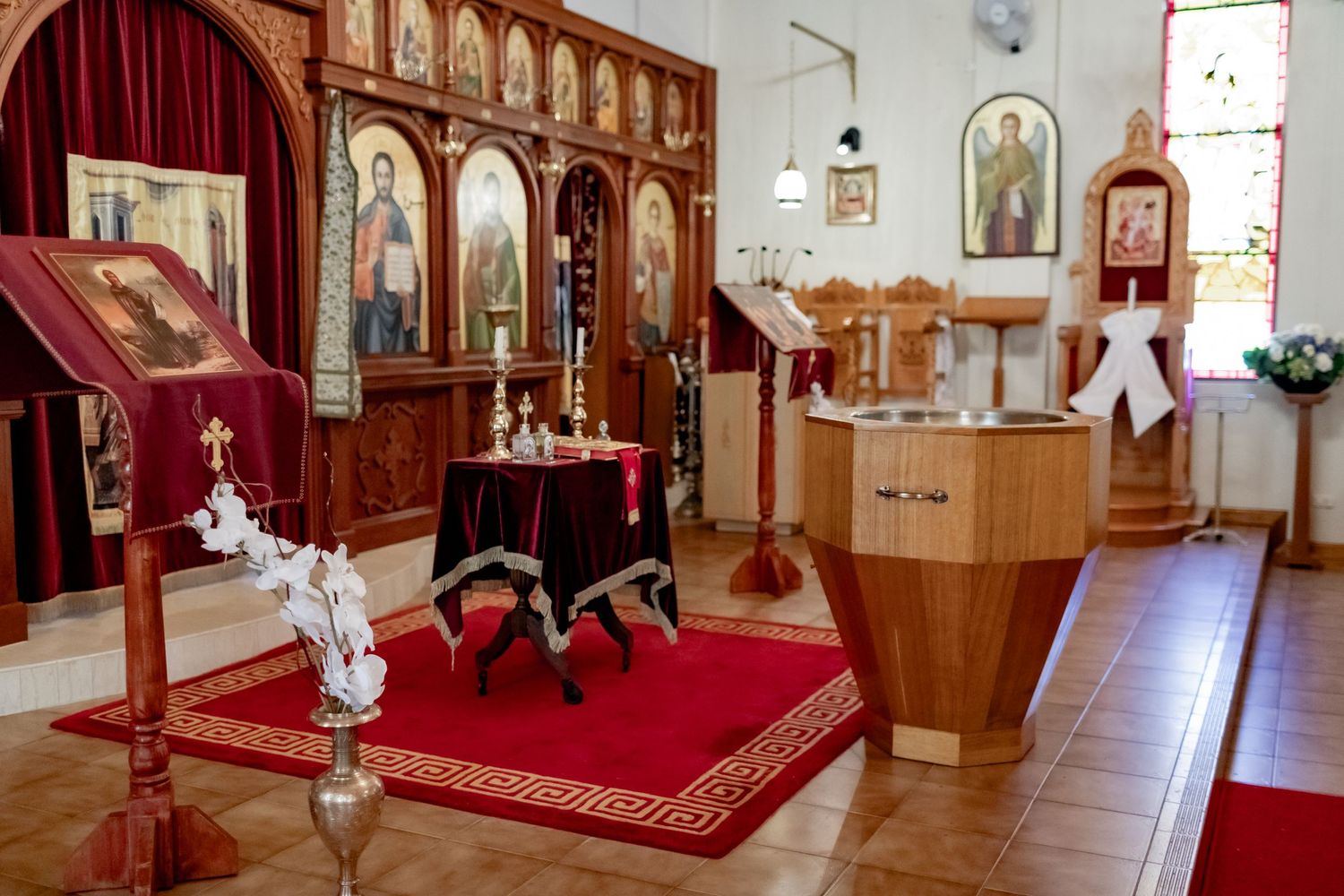Orthodox church interior with ornate wooden iconostasis and red carpet in the sanctuary.