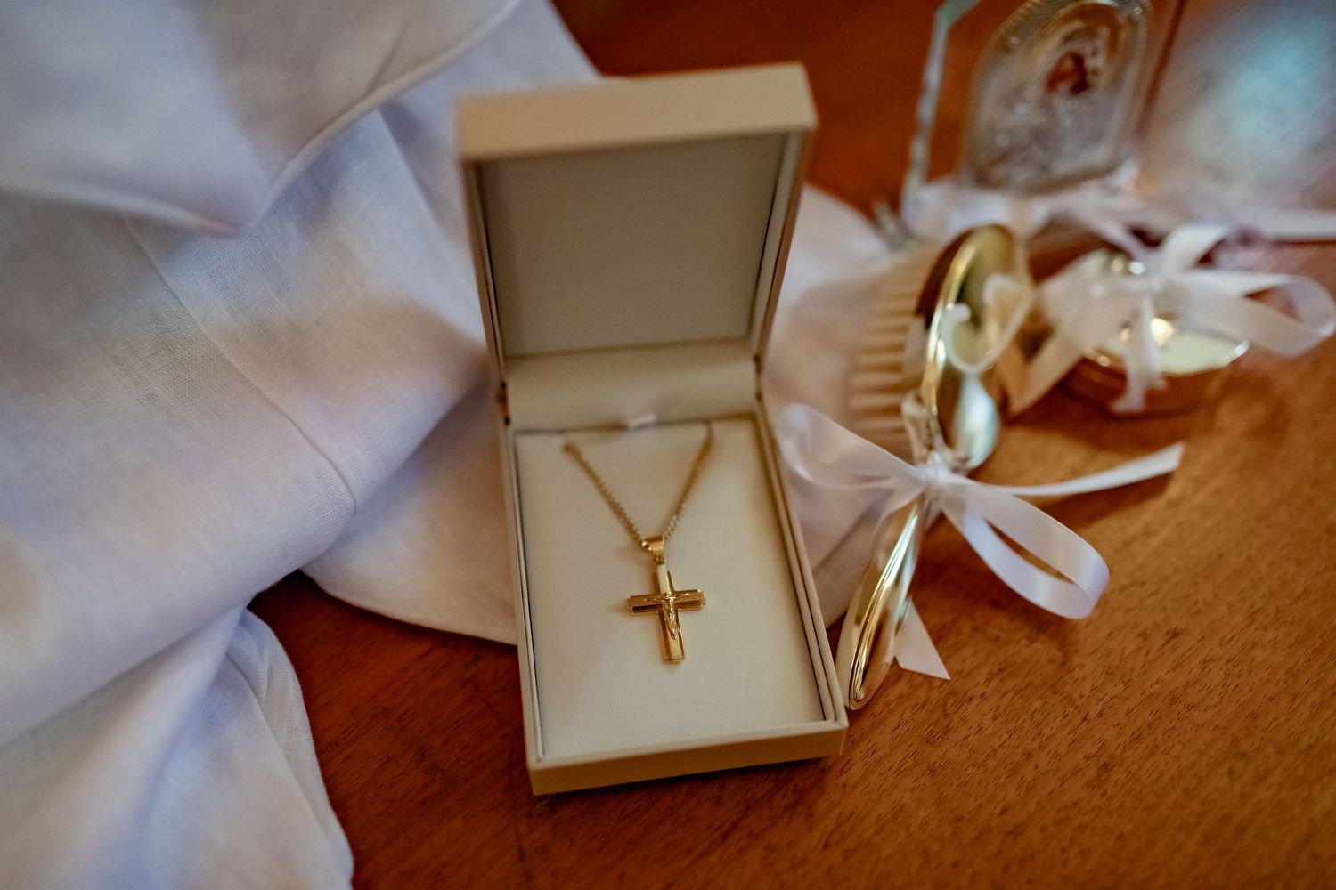 Gold cross necklace displayed in an open white jewelry box next to white fabric.
