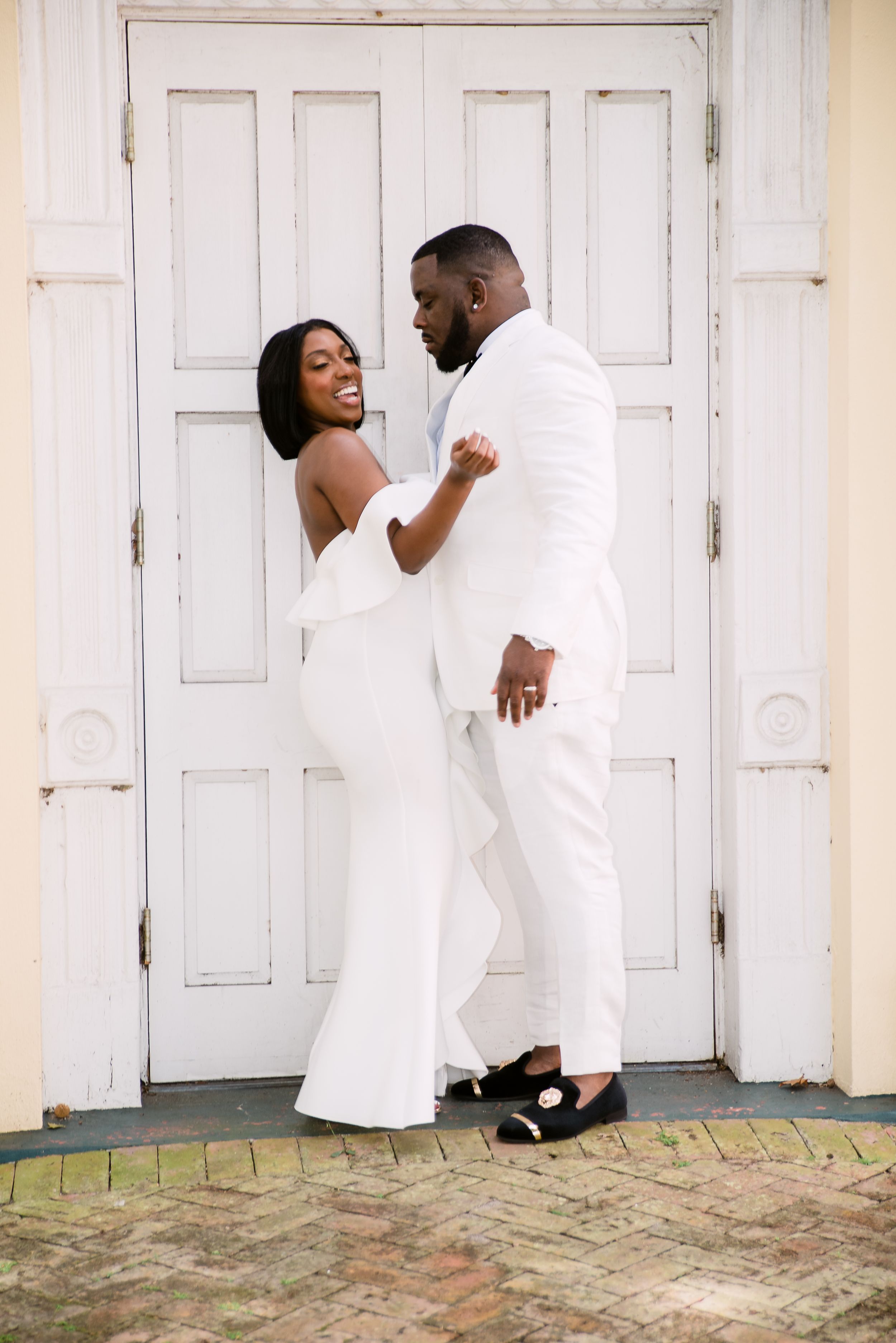 A romantic pose against a white paneled door shows coordinated white formal attire.