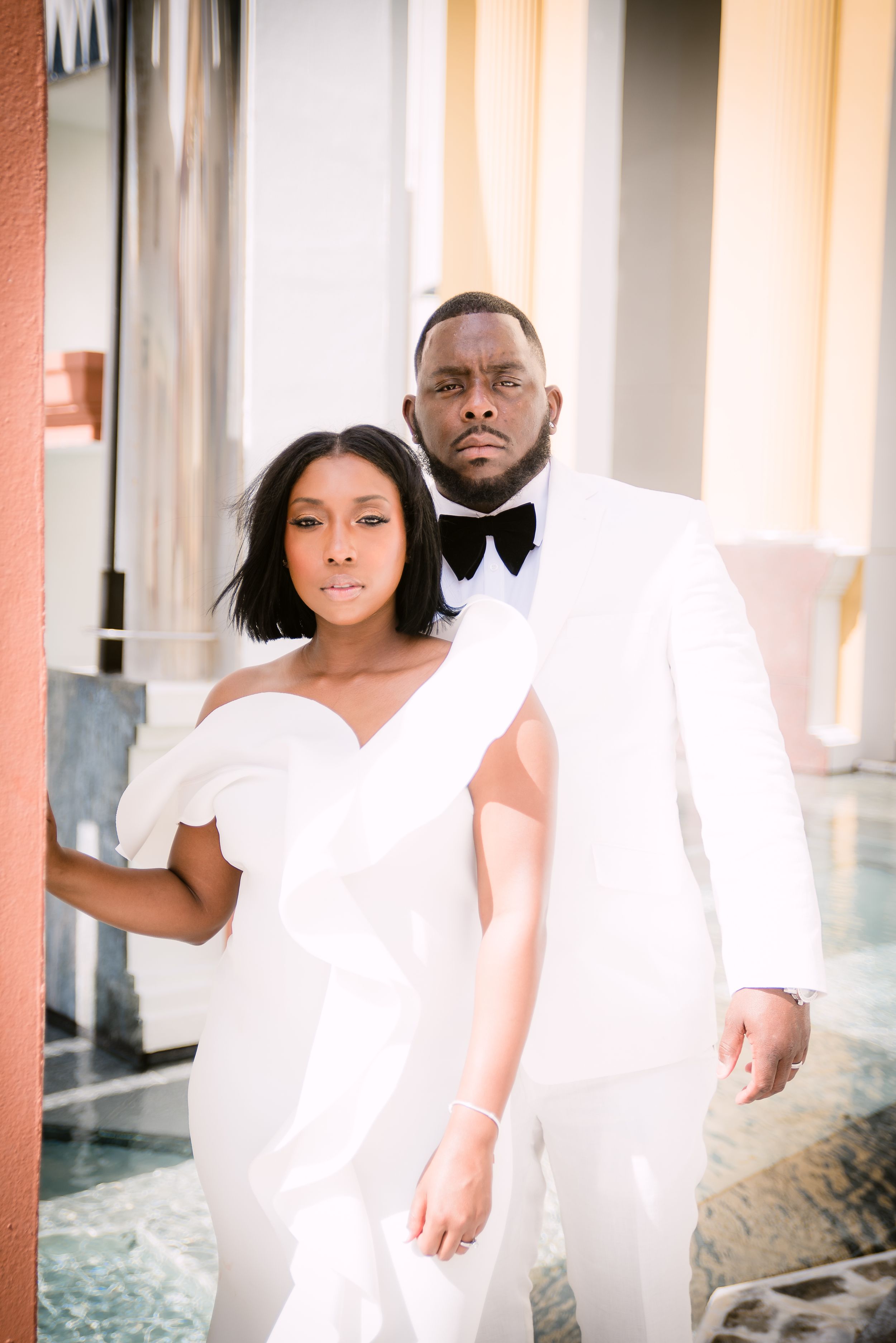 A couple in white attire share intimate poses against a white backdrop for artistic portrait photos.