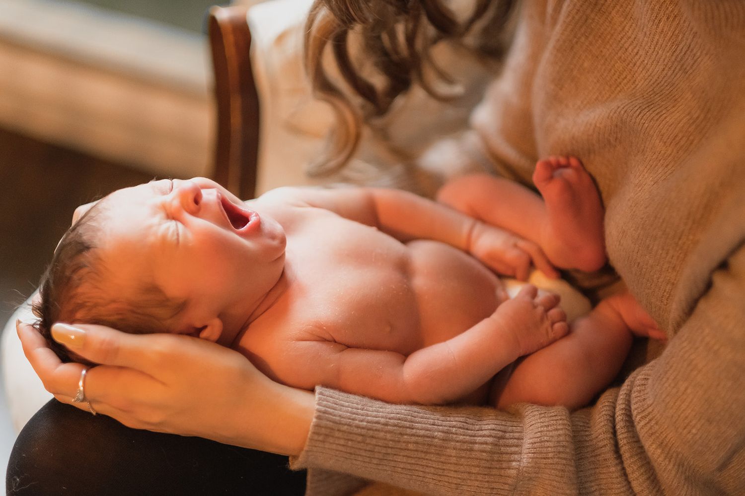 Precious newborn baby rests peacefully on soft hands wearing a cozy sweater.