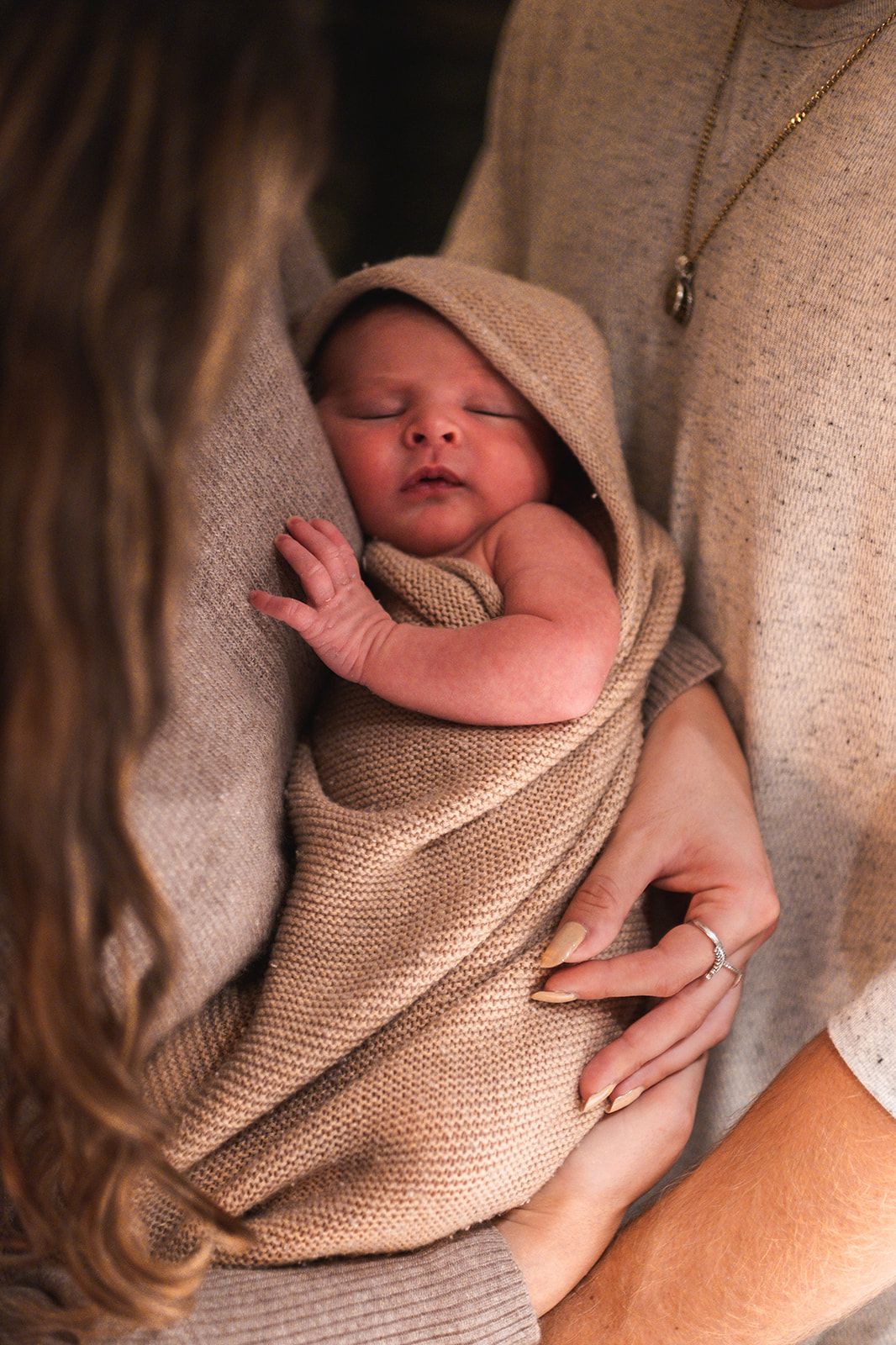 Sleeping newborn baby wrapped in soft beige knit blanket.