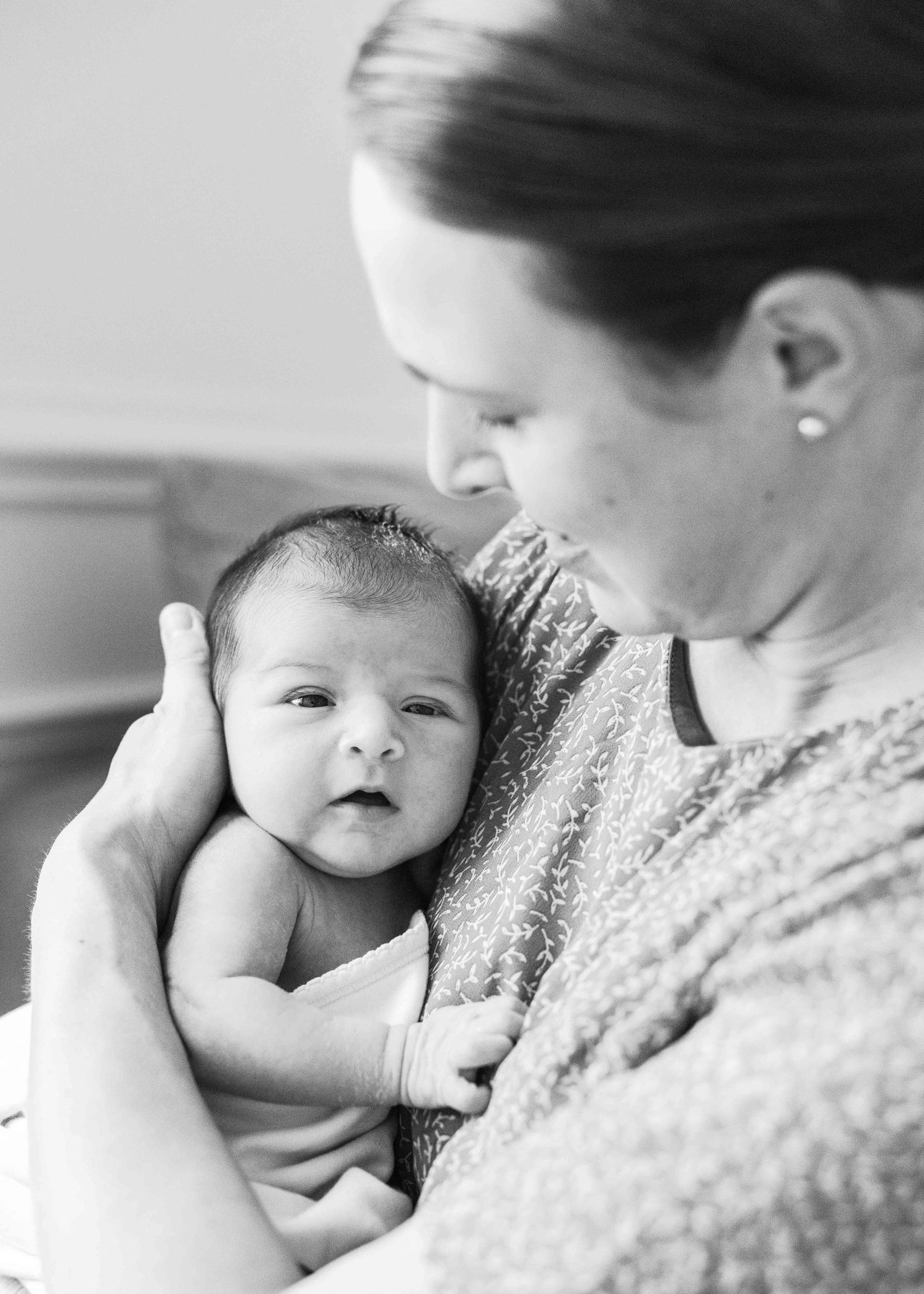 A tender black and white portrait of a parent cradling a newborn baby against their chest in a sweater.