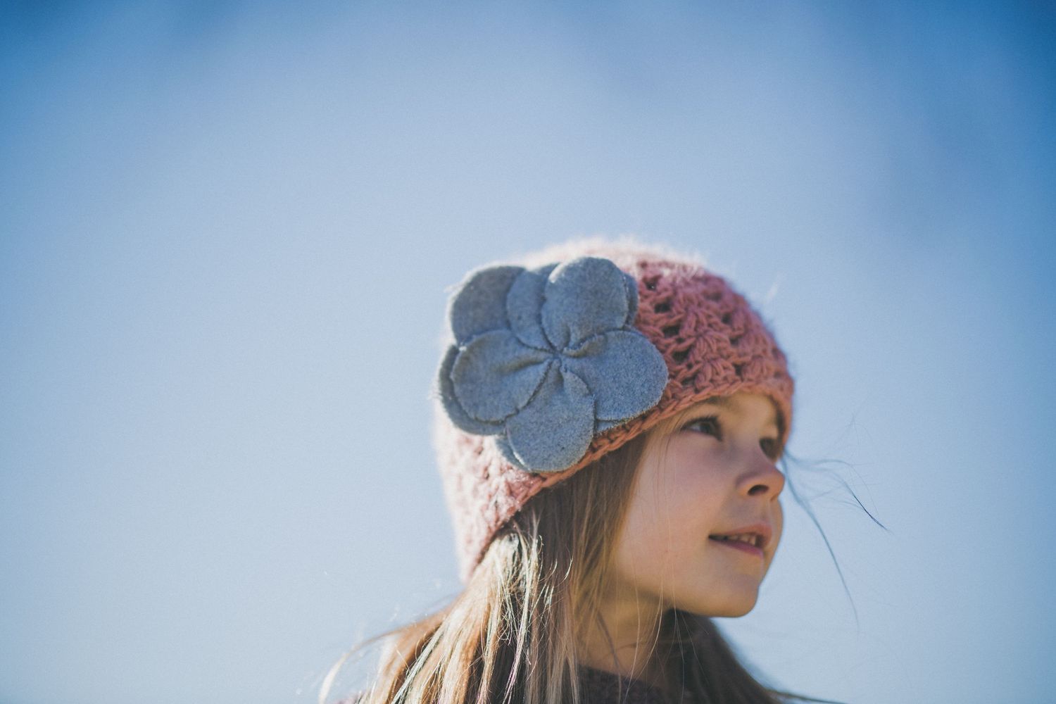 Girl in crotchet pink hat with grey flower with the blank blue sky behind her