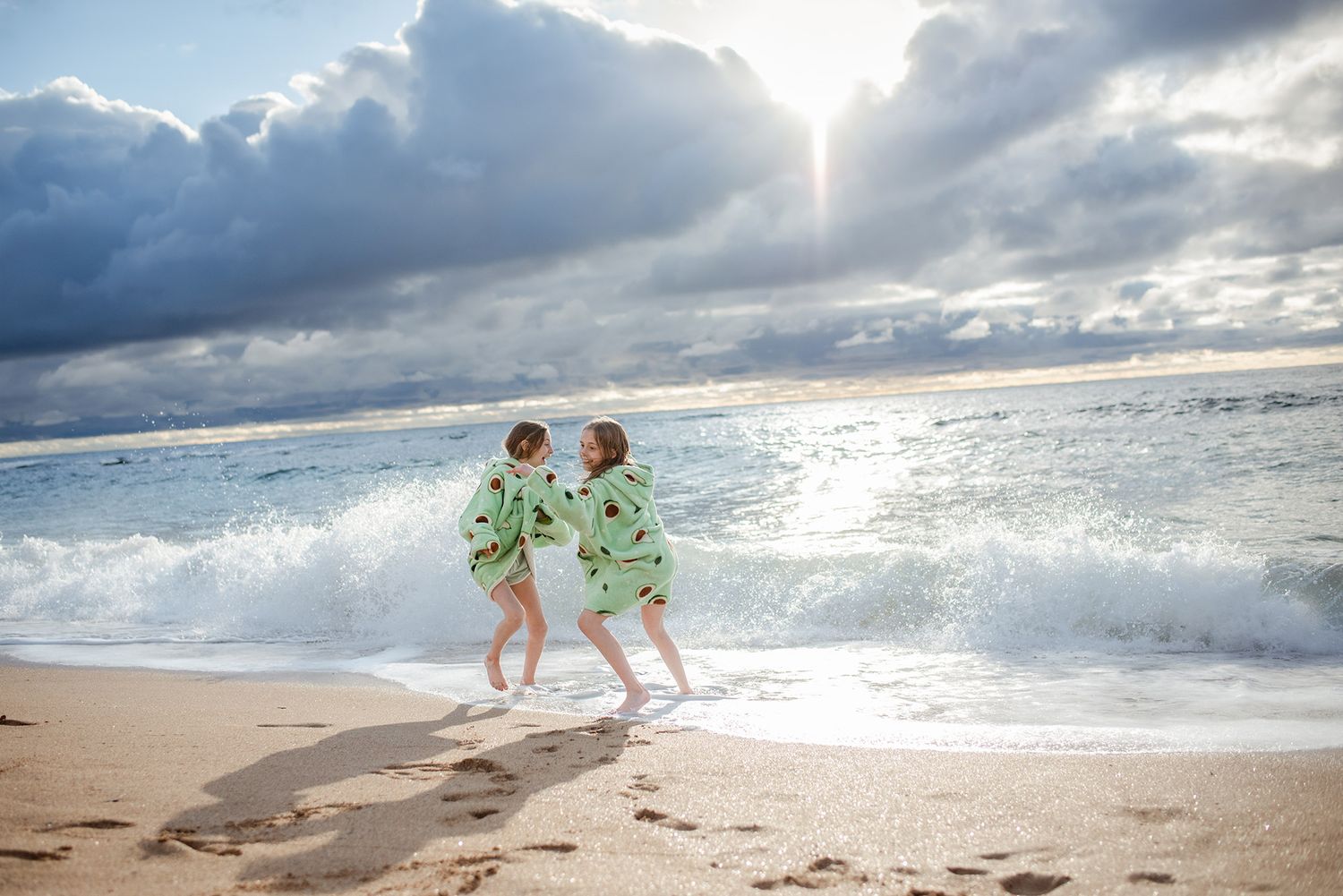 Children in matching outfits play on beach with crashing waves and dramatic sky.