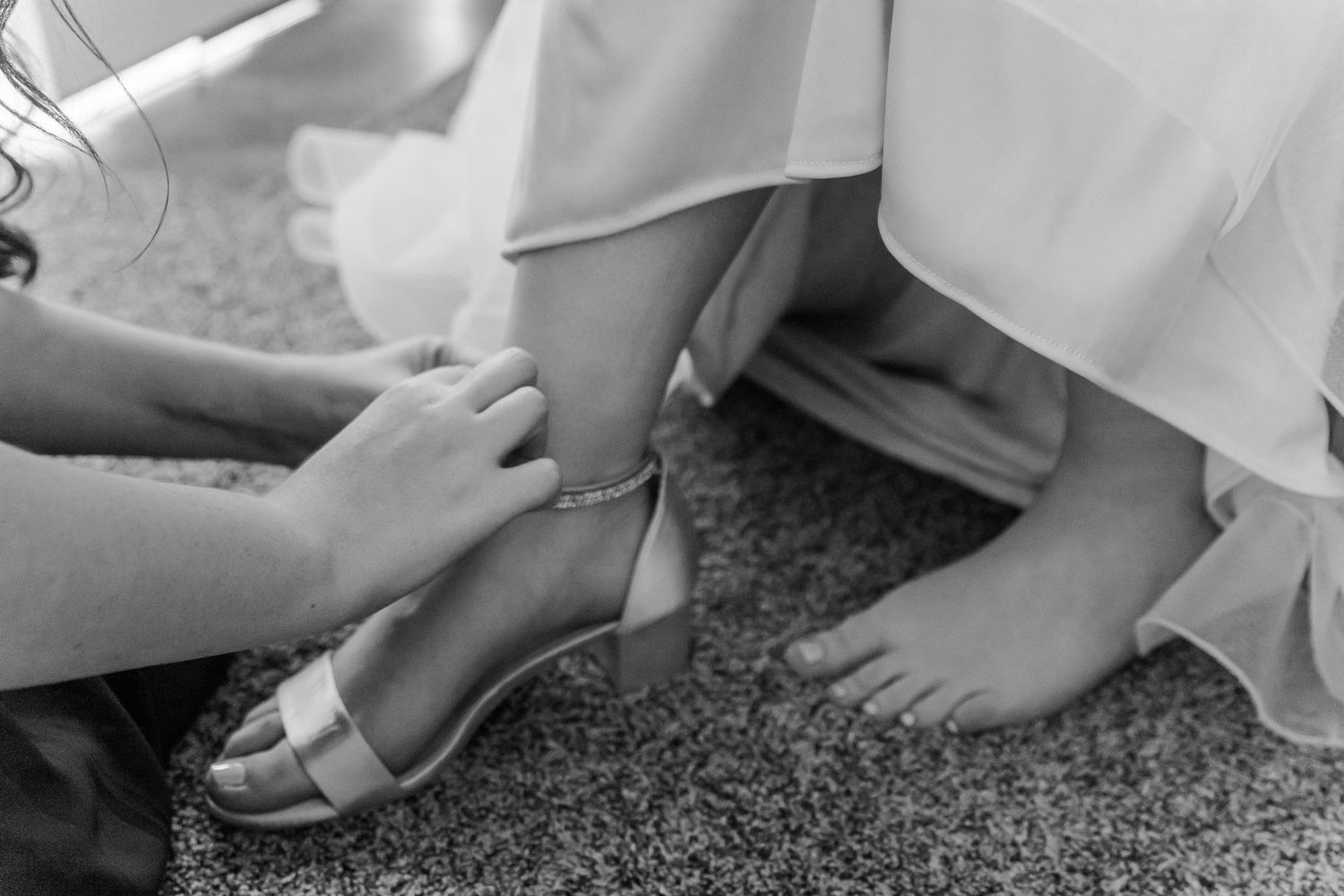 Black and white image of hands adjusting a wedding shoe strap.