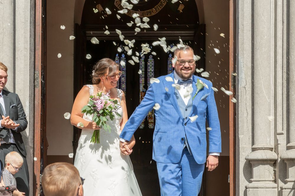 Happy couple exiting church as guests throw flower petals in celebration.