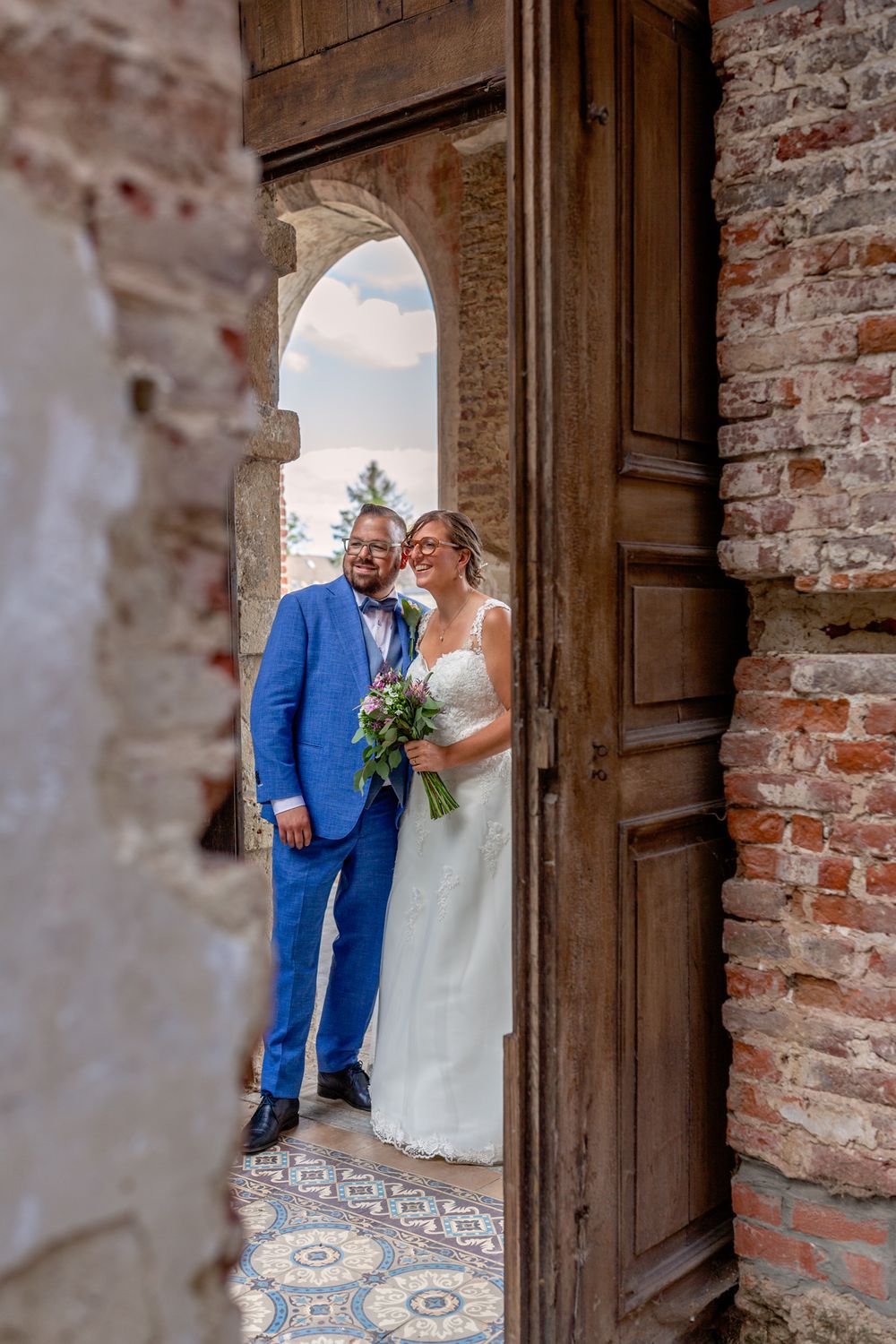 Wedding couple standing in rustic brick doorway of historic building.