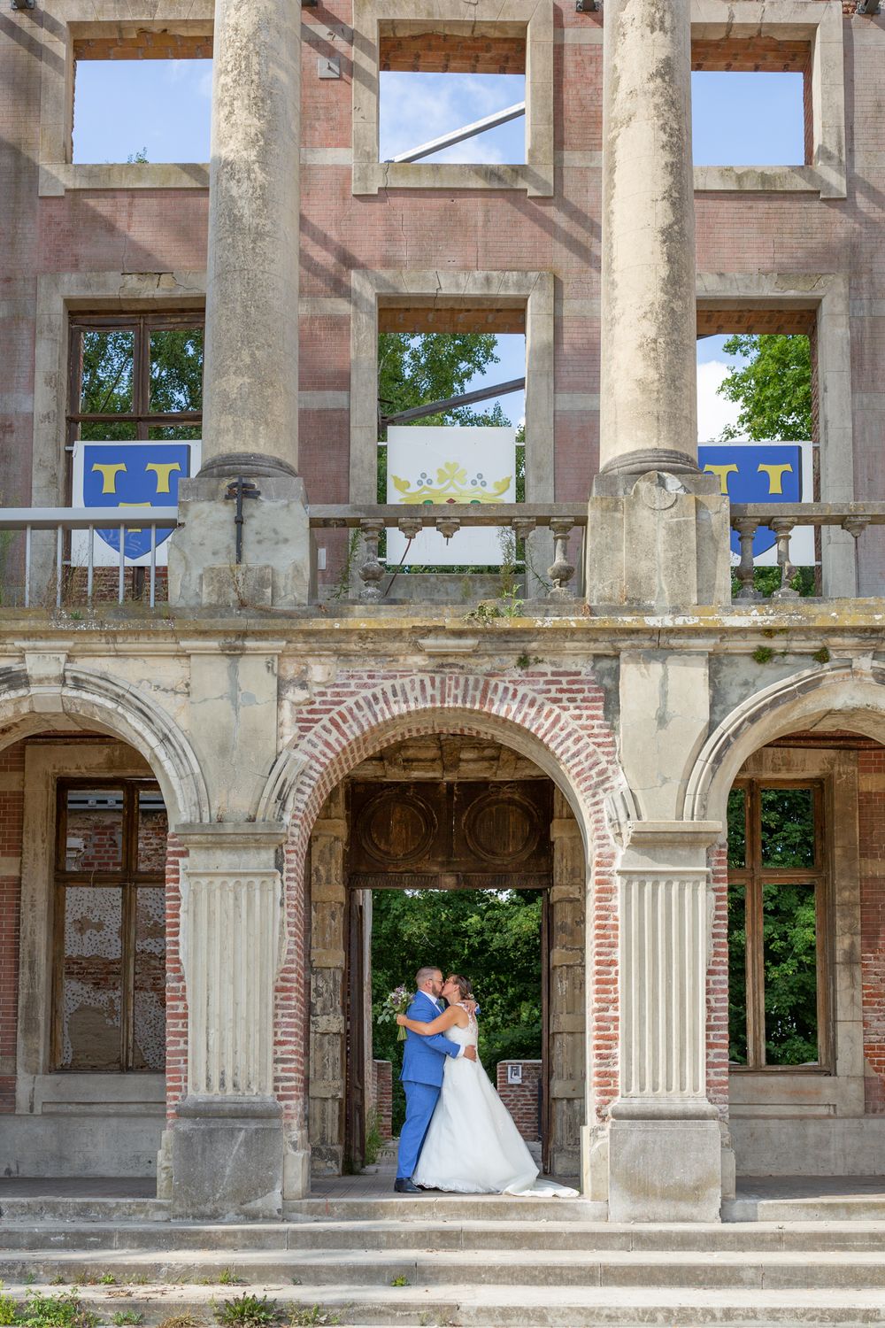 A wedding couple embraces in a grand architectural doorway with classical columns.