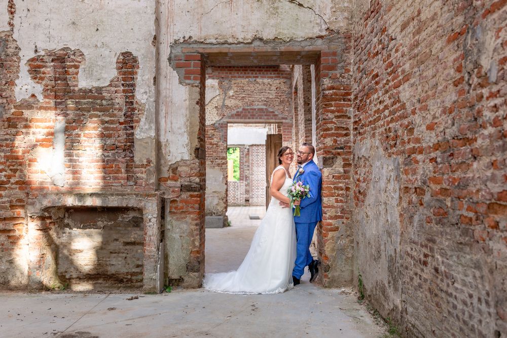 A bride and groom stand in an archway of weathered brick walls with dramatic lighting.