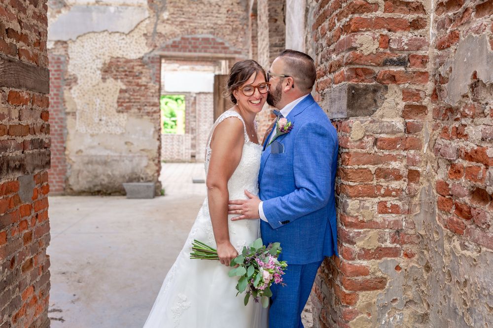 A romantic wedding moment captured between a couple in front of aged brick walls.