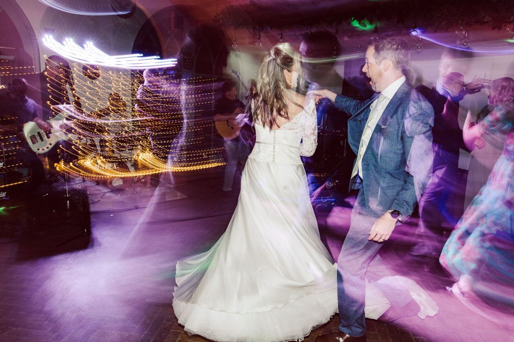 Wedding reception dance floor filled with guests under purple mood lighting.