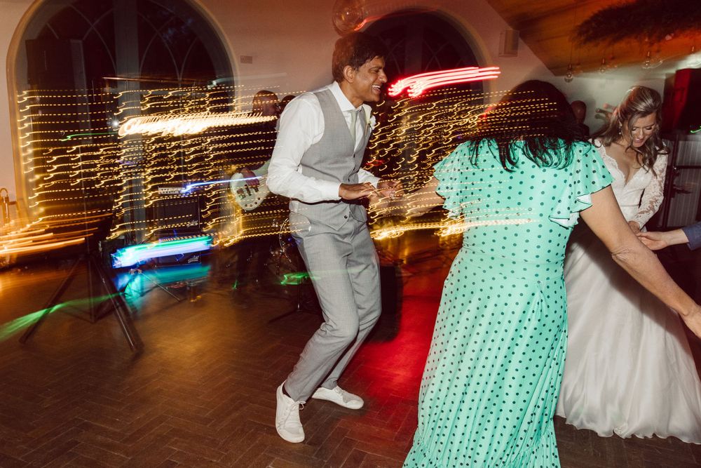 Wedding celebration features dancing guests in formal attire under colorful venue lighting.