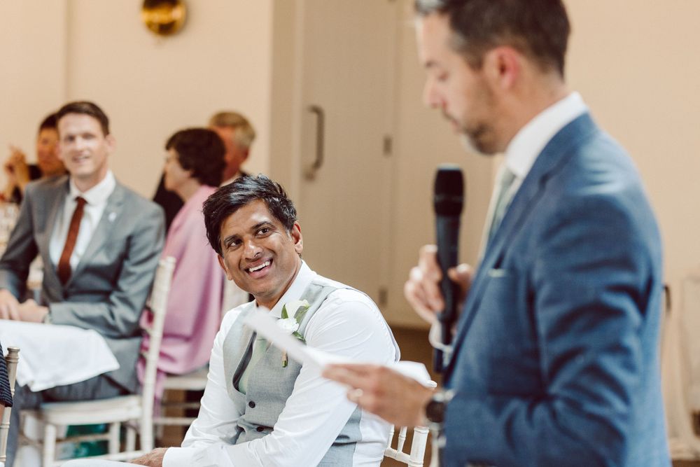 Wedding reception guests seated at tables listen attentively to speeches during the celebration.