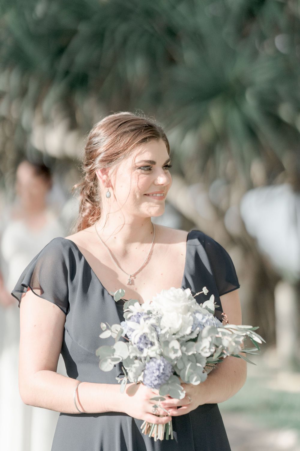 smiling brunette with hair half up carrying blue and white bouquet and wearing dark blue gown
