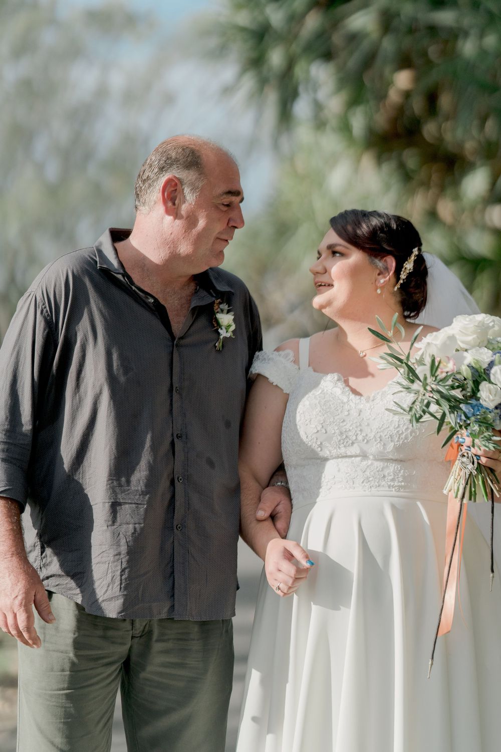 plus size bride with brunette hair in updo smiling at father in dark shirt and pants