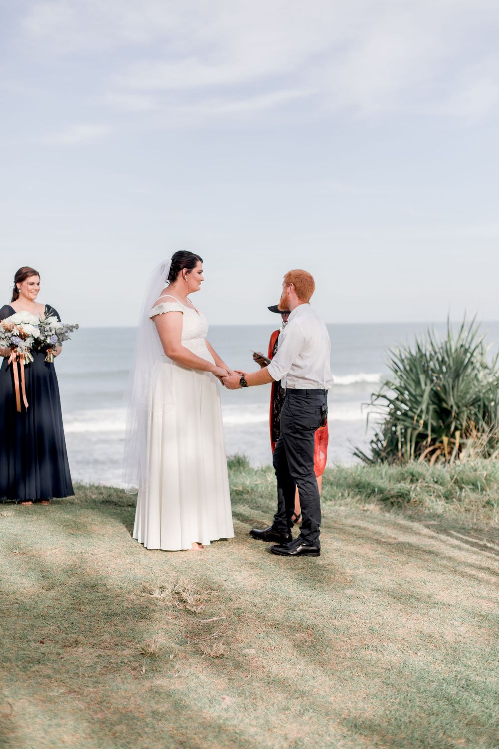 plus size bride with brunette hair in updo and veil holding hands with redheaded groom in white shirt and dark pants on