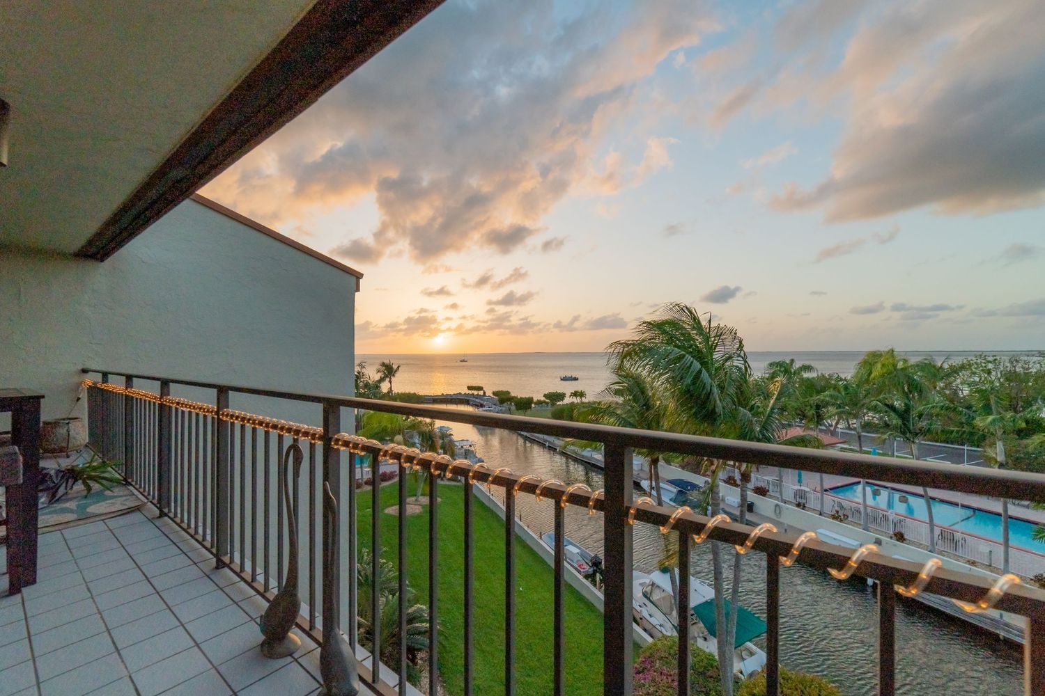 Luxury oceanfront balcony with stunning sunset view over tropical pool and palm trees.