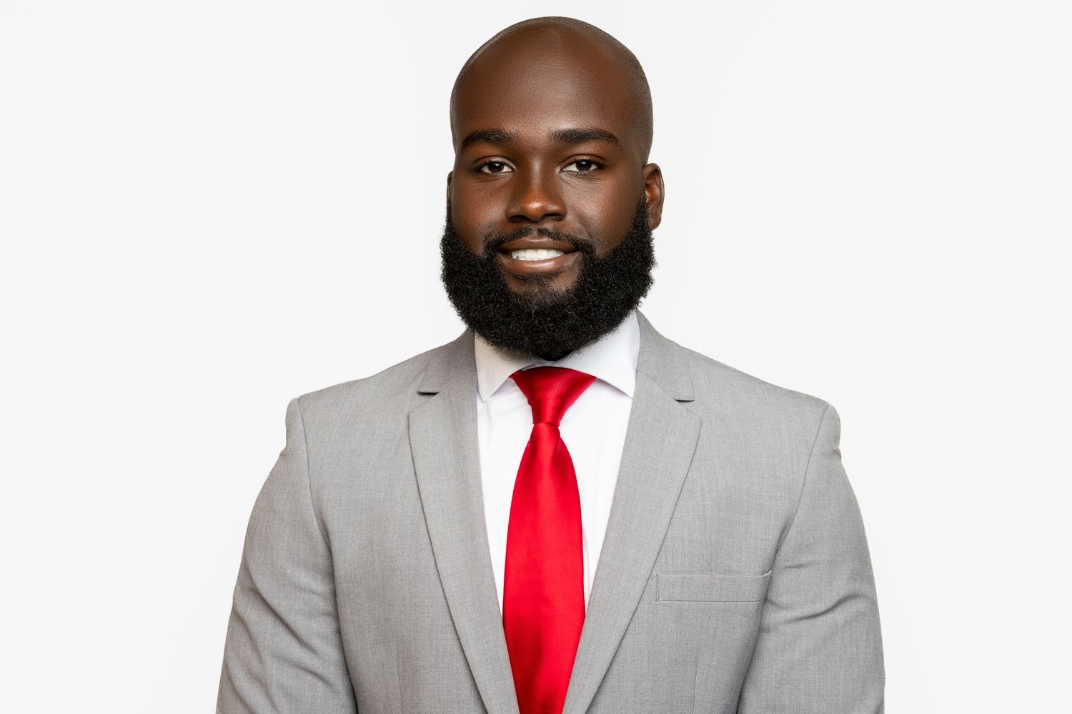 Professional Black man in gray suit and red tie smiling confidently against white background.