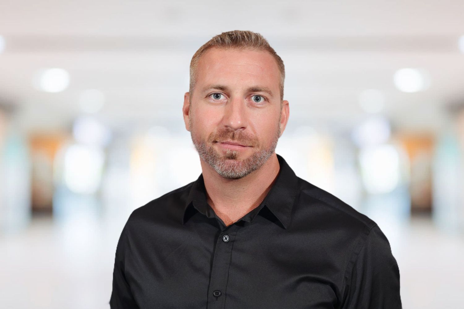 Professional man in black shirt smiling in a bright modern office setting.