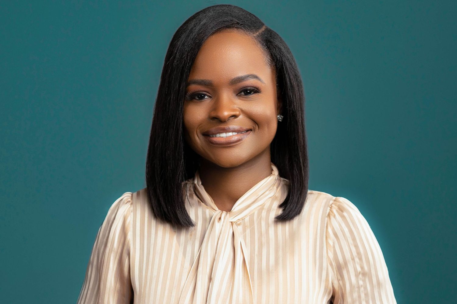 Professional Black woman with straight bob haircut smiling in striped blouse on teal background.
