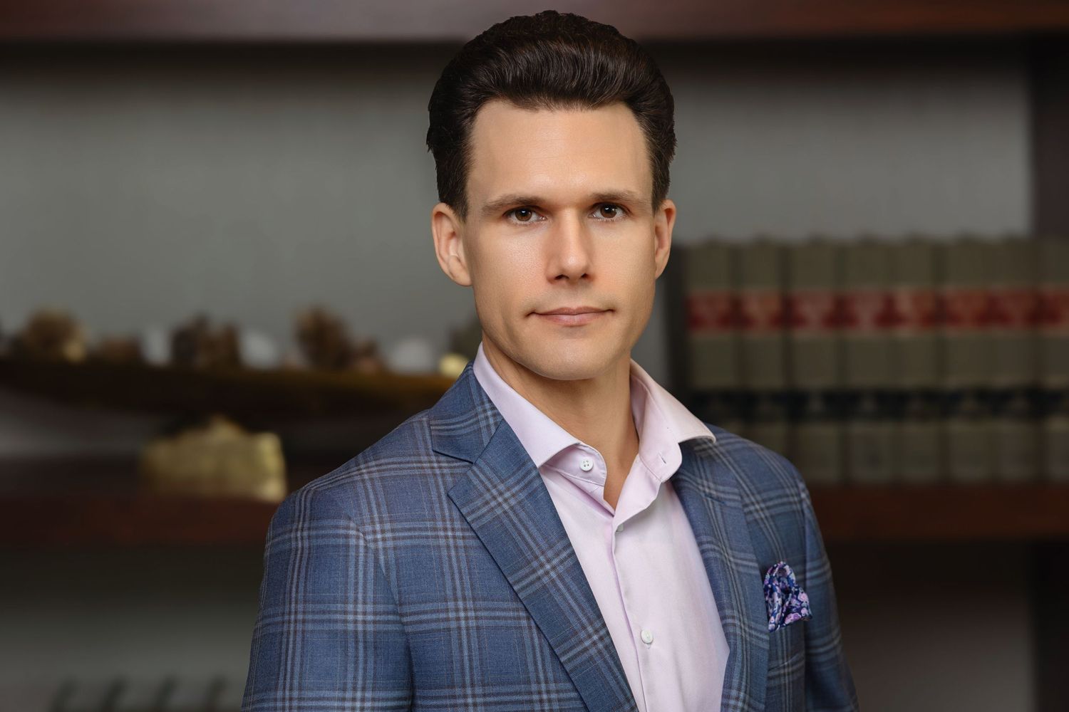 Professional portrait of a man in a plaid blazer with a pocket square in front of law books.