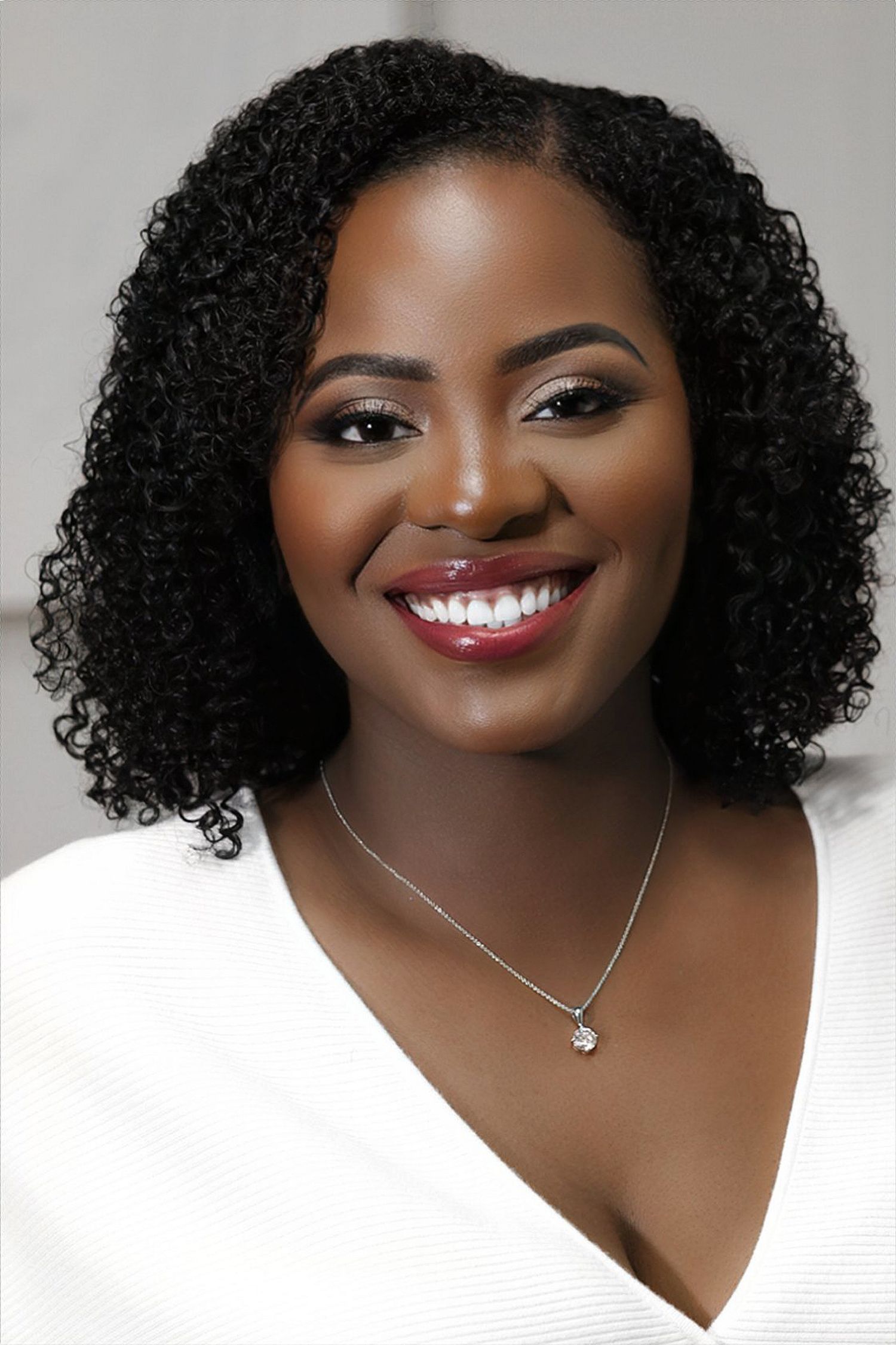 Elegant Black woman with curly hair and silver necklace smiling in white top closeup.
