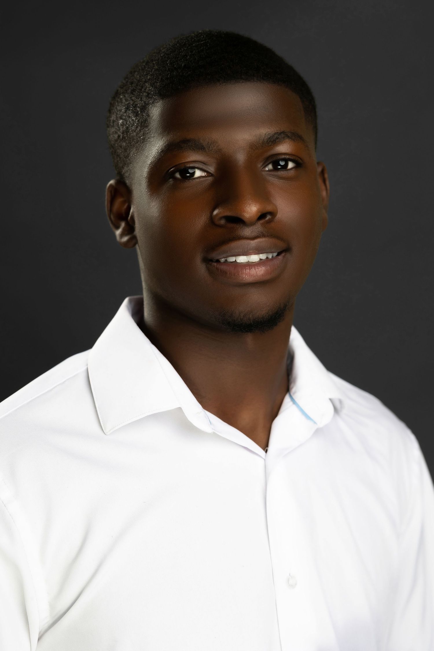 Young man in white dress shirt with subtle smile against dark background.