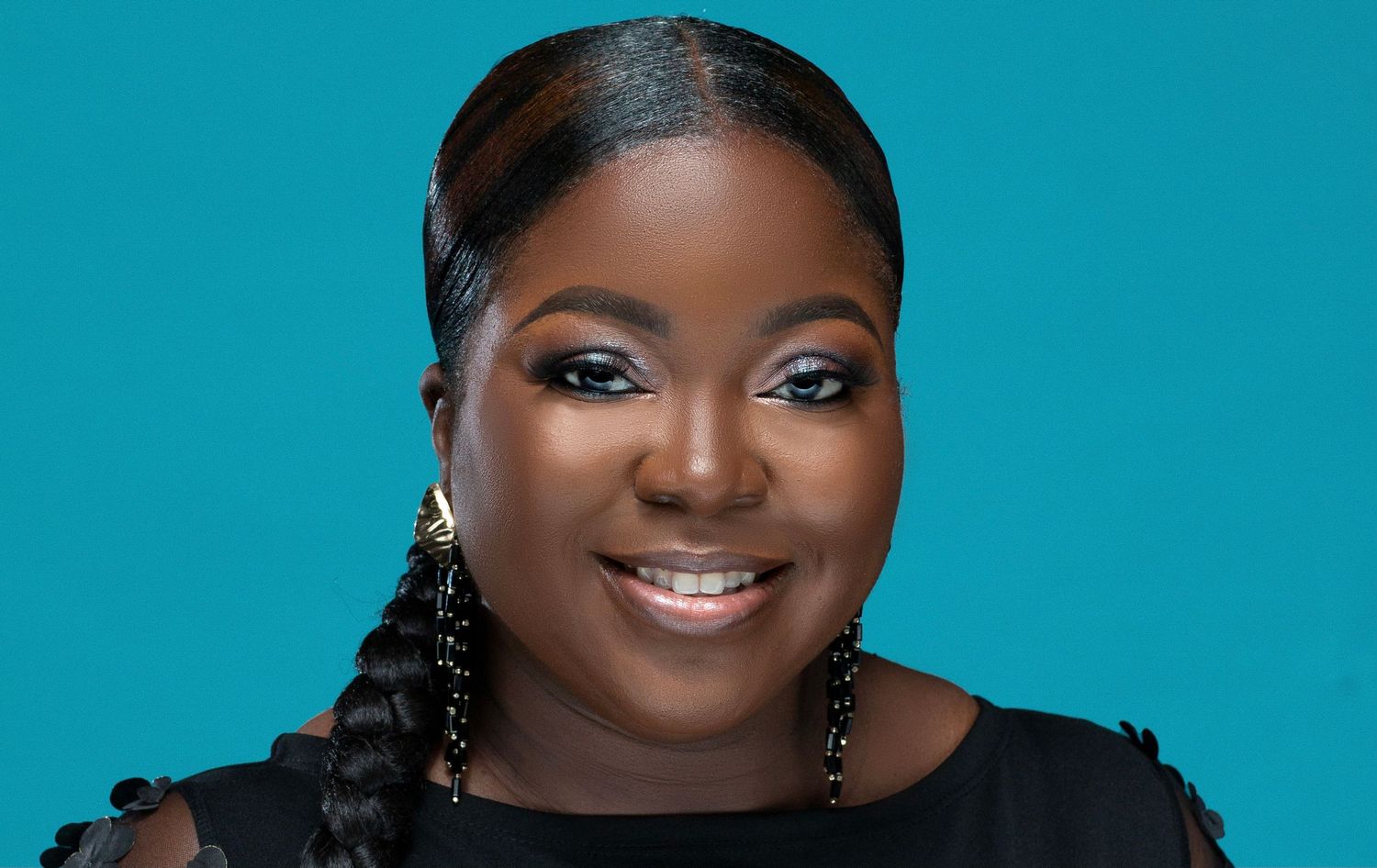 Smiling Black woman with braids and drop earrings in black top against bright teal background.