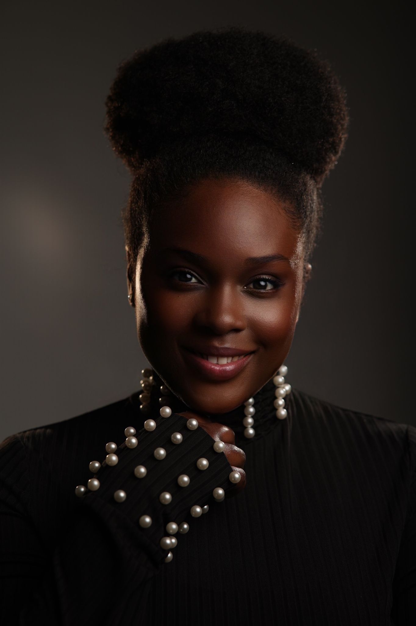 Elegant woman in black outfit with pearl accessories and natural updo hairstyle.
