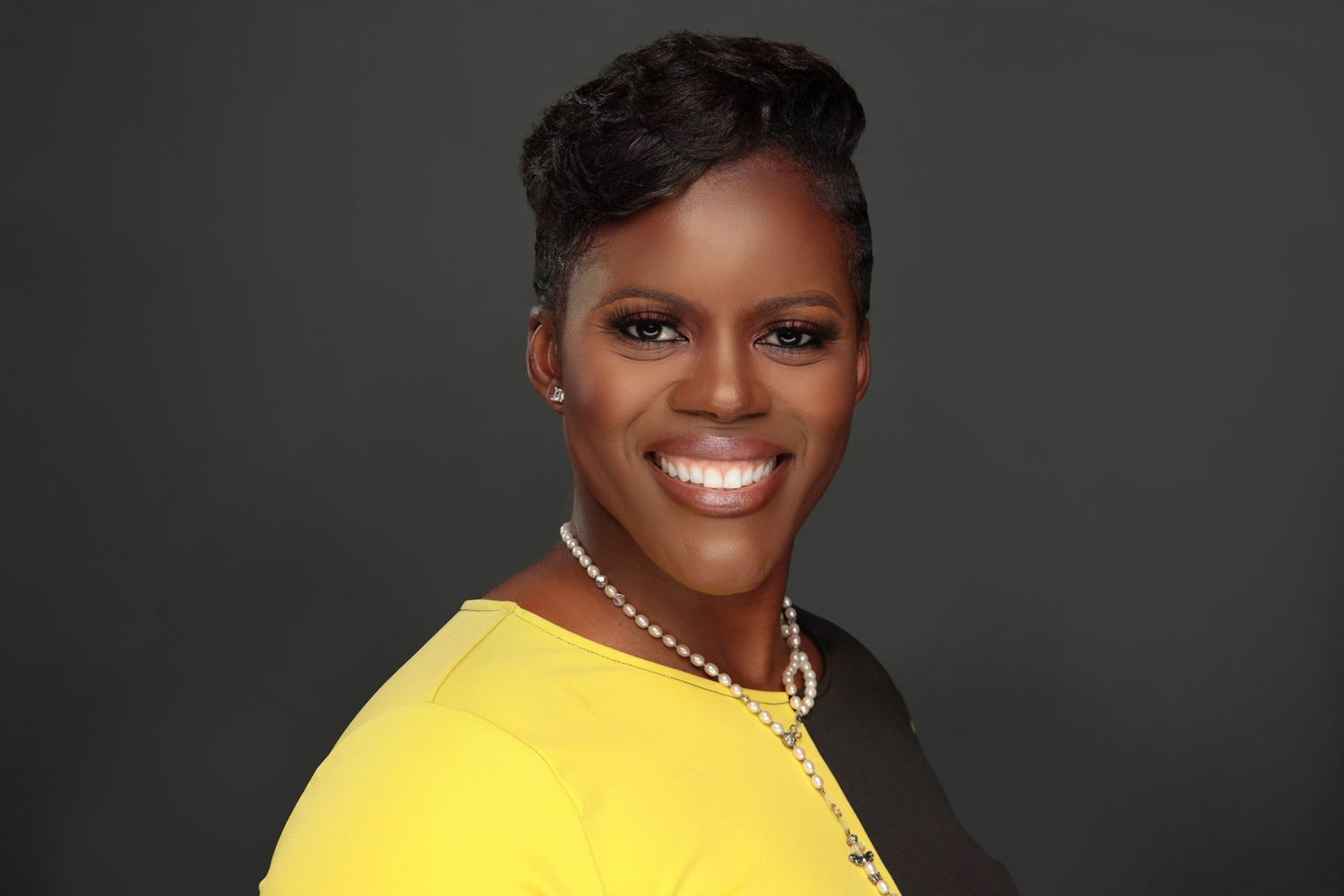 Smiling Black woman in yellow blazer with short hair poses for vibrant professional headshot.