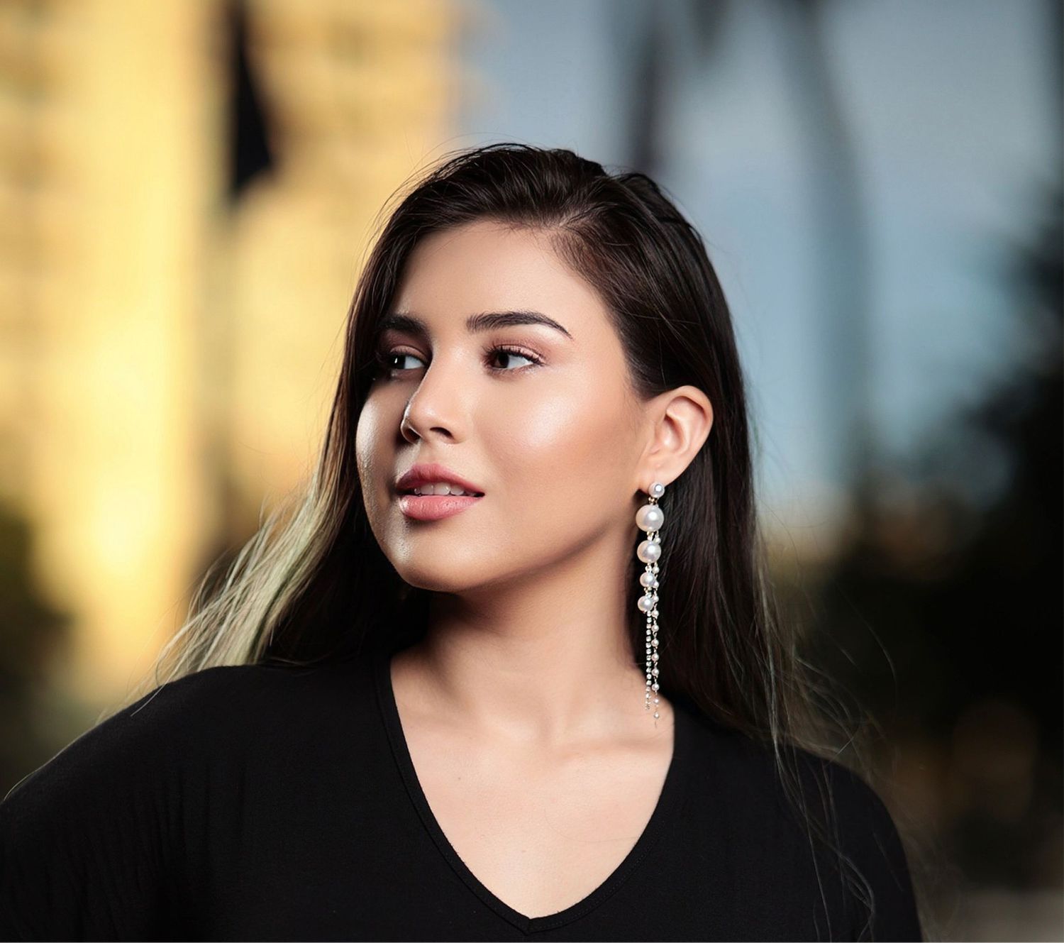 Young woman with long dark hair wearing dangling crystal earrings and black top in urban setting.