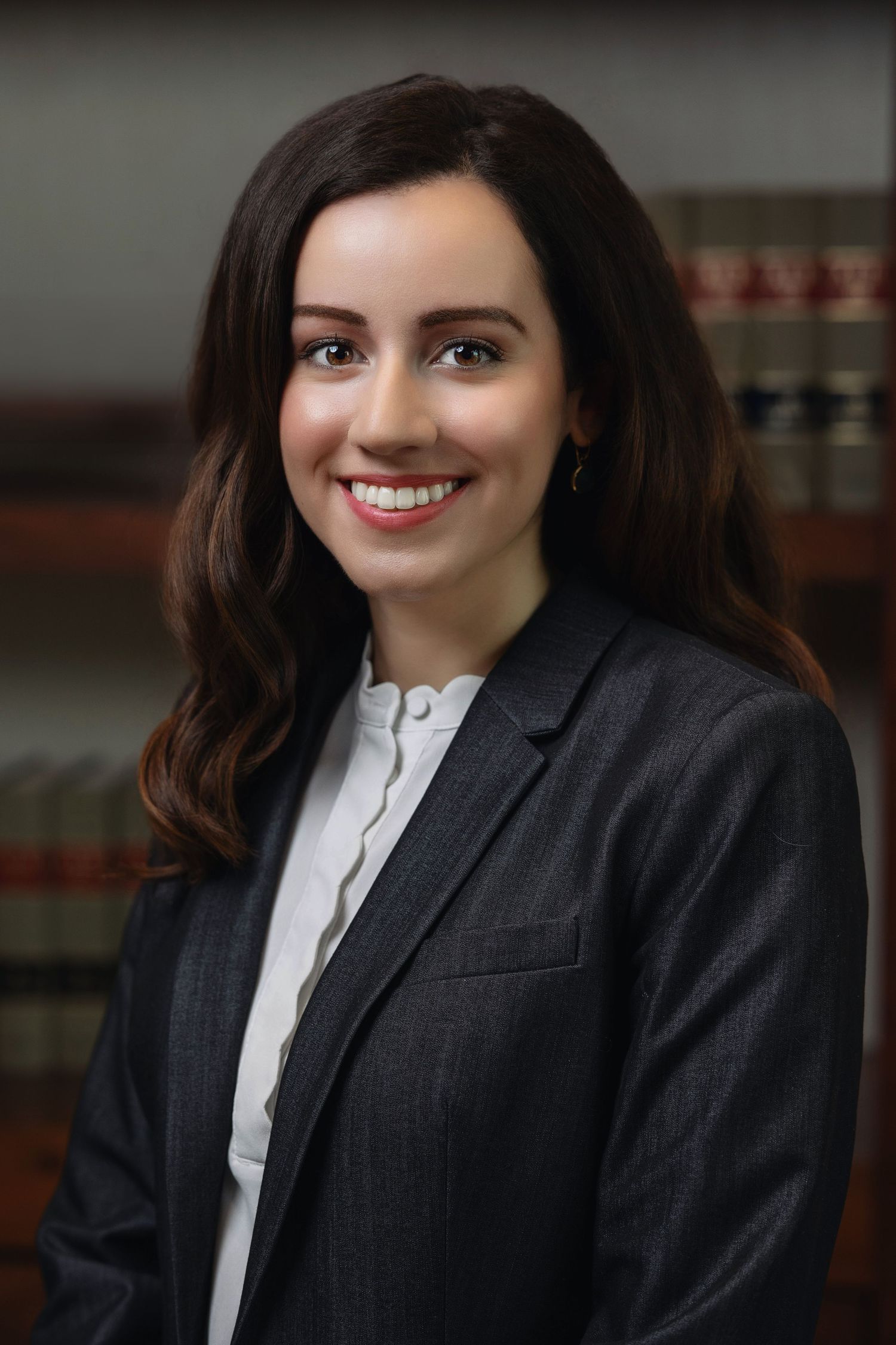 Smiling young female lawyer in gray blazer before legal bookshelf.