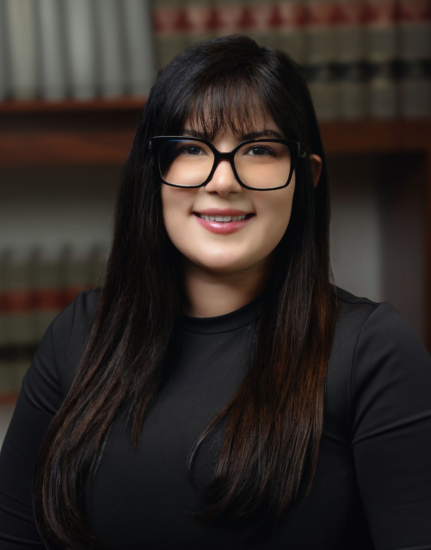 Young woman with glasses in black top posing before law library shelves.